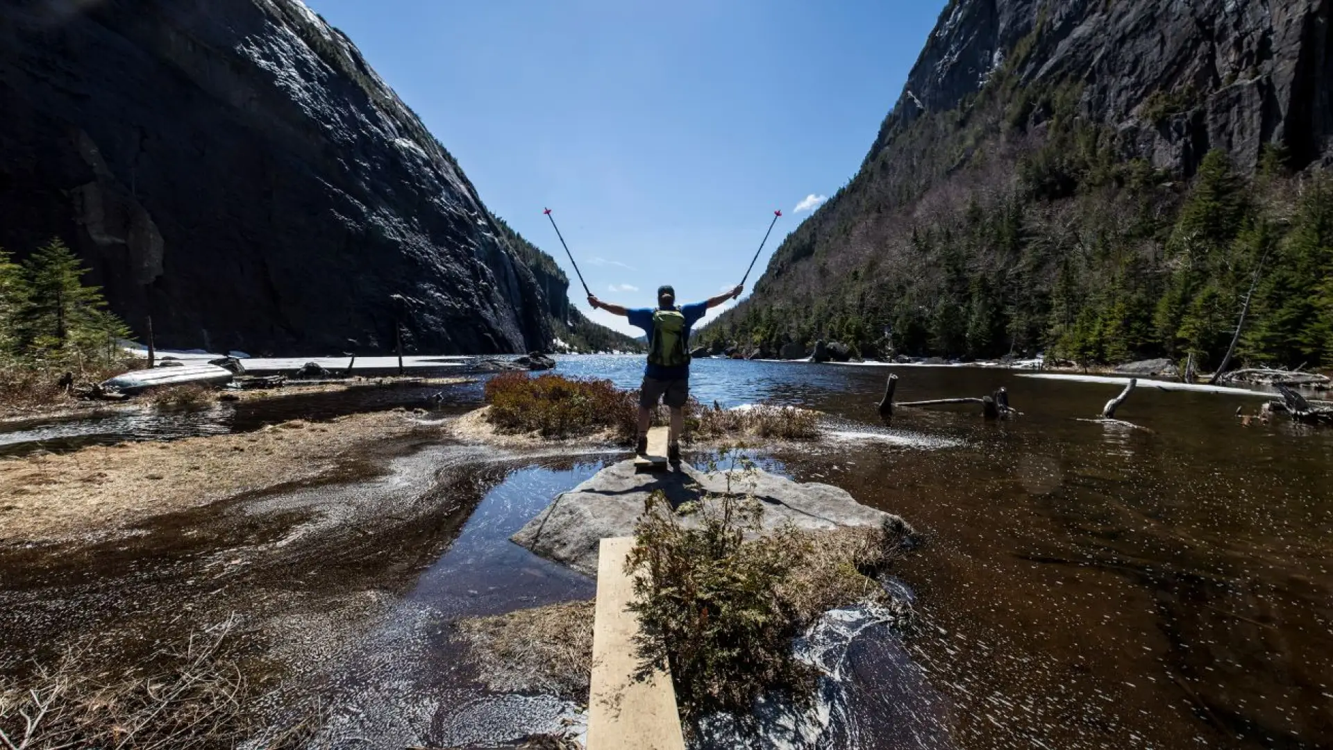 A man posing on the shore of Avalanche Lake while spring hiking in the Adirondacks.