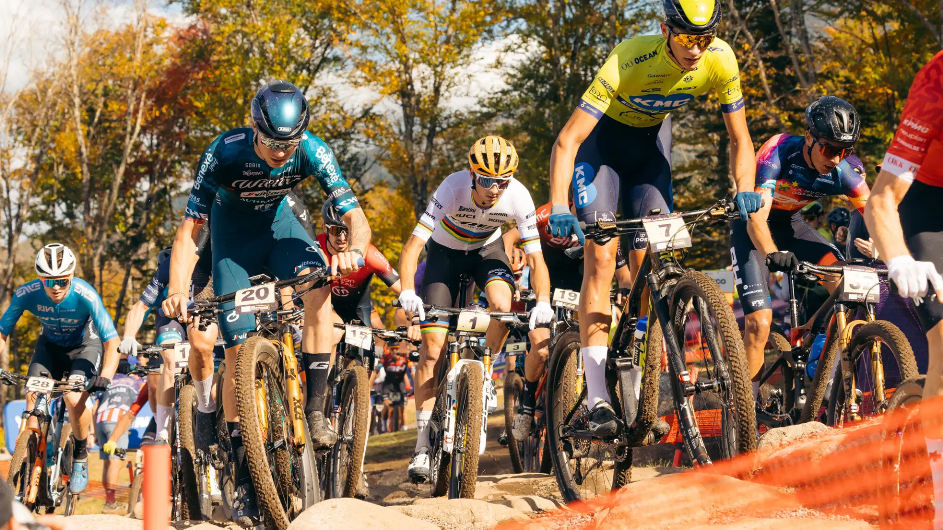 Pack of mountain bikers in colorful uniforms racing on dirt trail