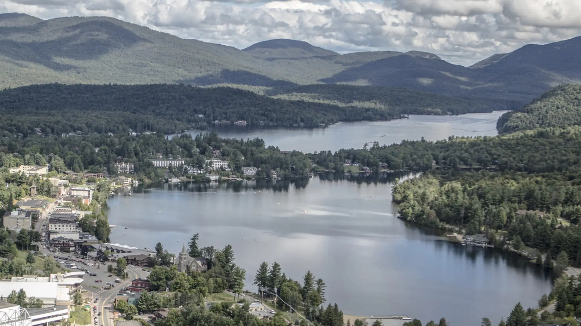 An aerial view of the village of Lake Placid, lined with shops and restaurants, and adjacent to Lake Placid lake and Mirror Lake.