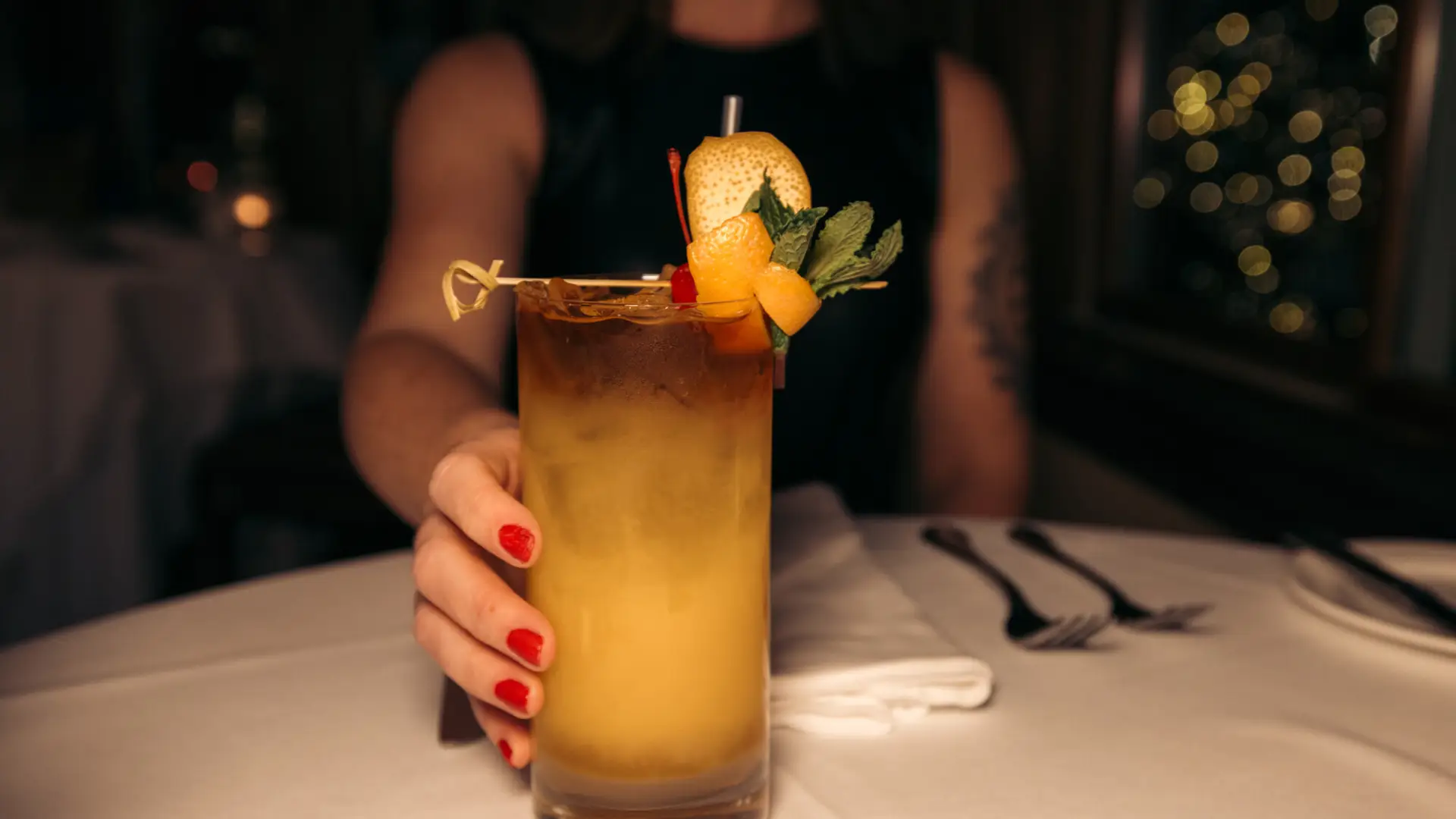 woman's hand with red  painted fingernails holds glass with yellow fruity cocktail