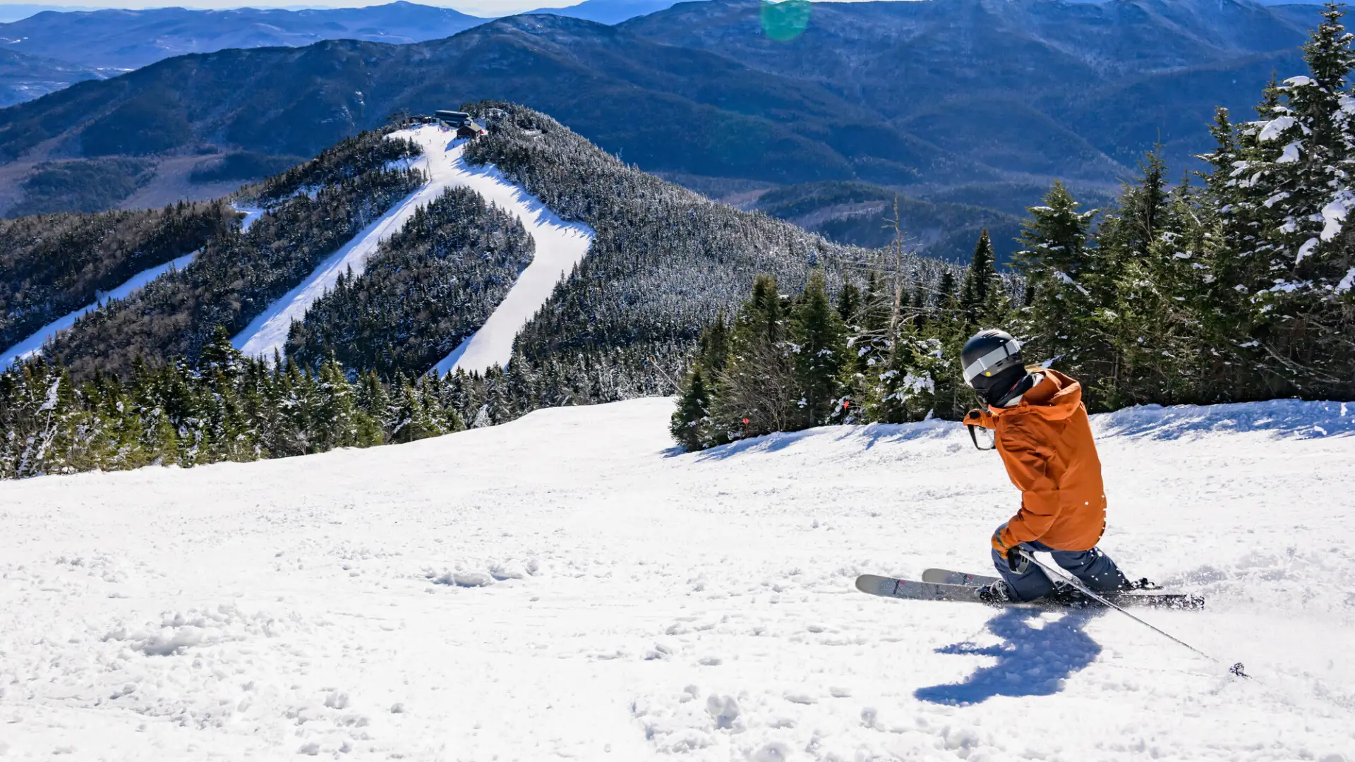 A man in an orange jacket skis down a mountain in winter. 