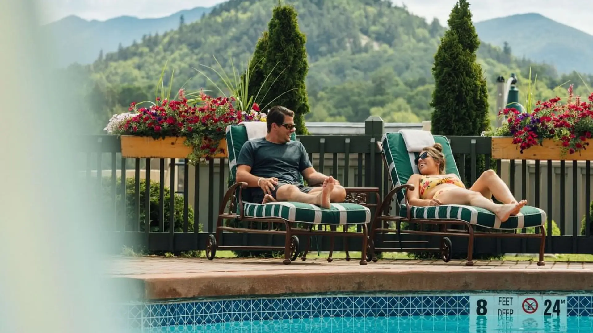 A couple lounges by the outdoor pool with the mountains in the distance