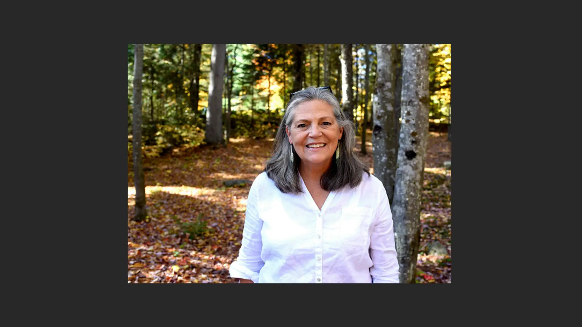 A woman smiling at the camera in the forest.