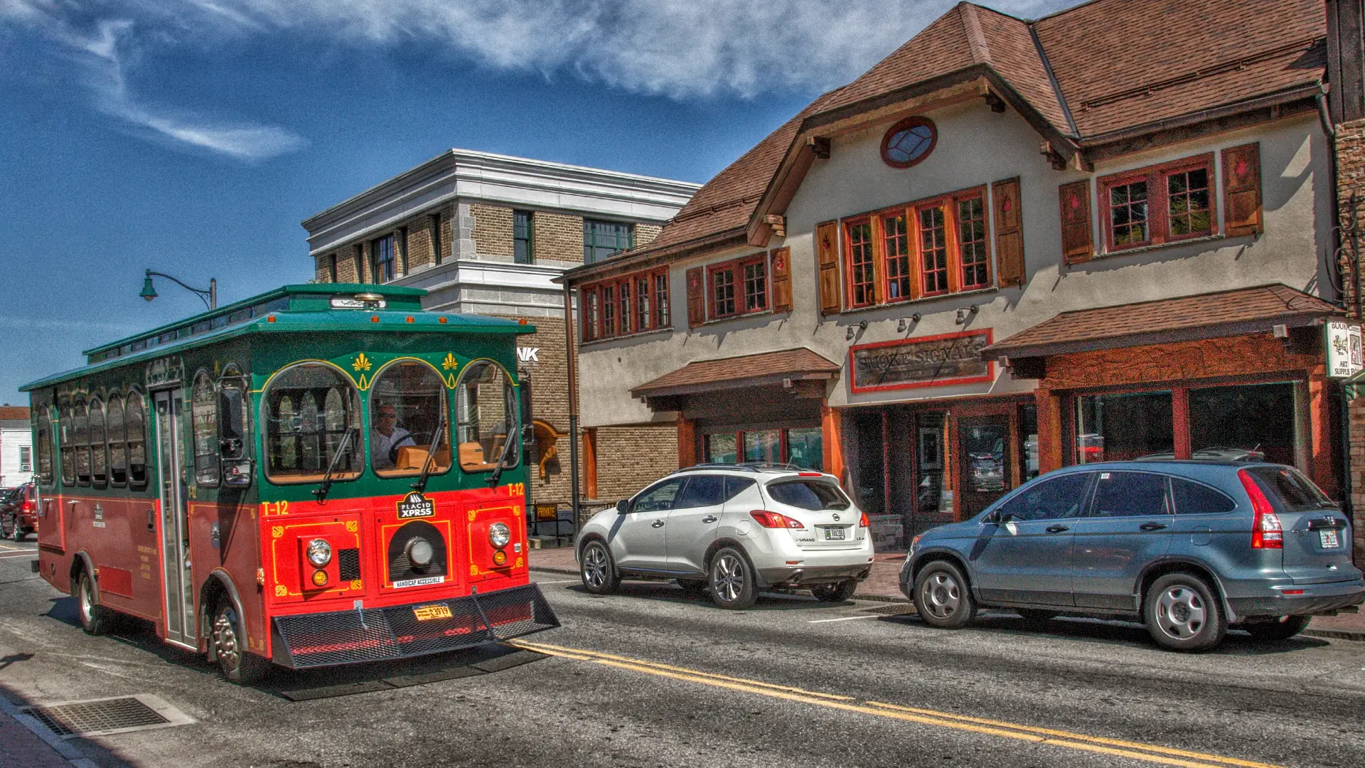A trolley bus drives on a quaint street past a barbecue restaurant.