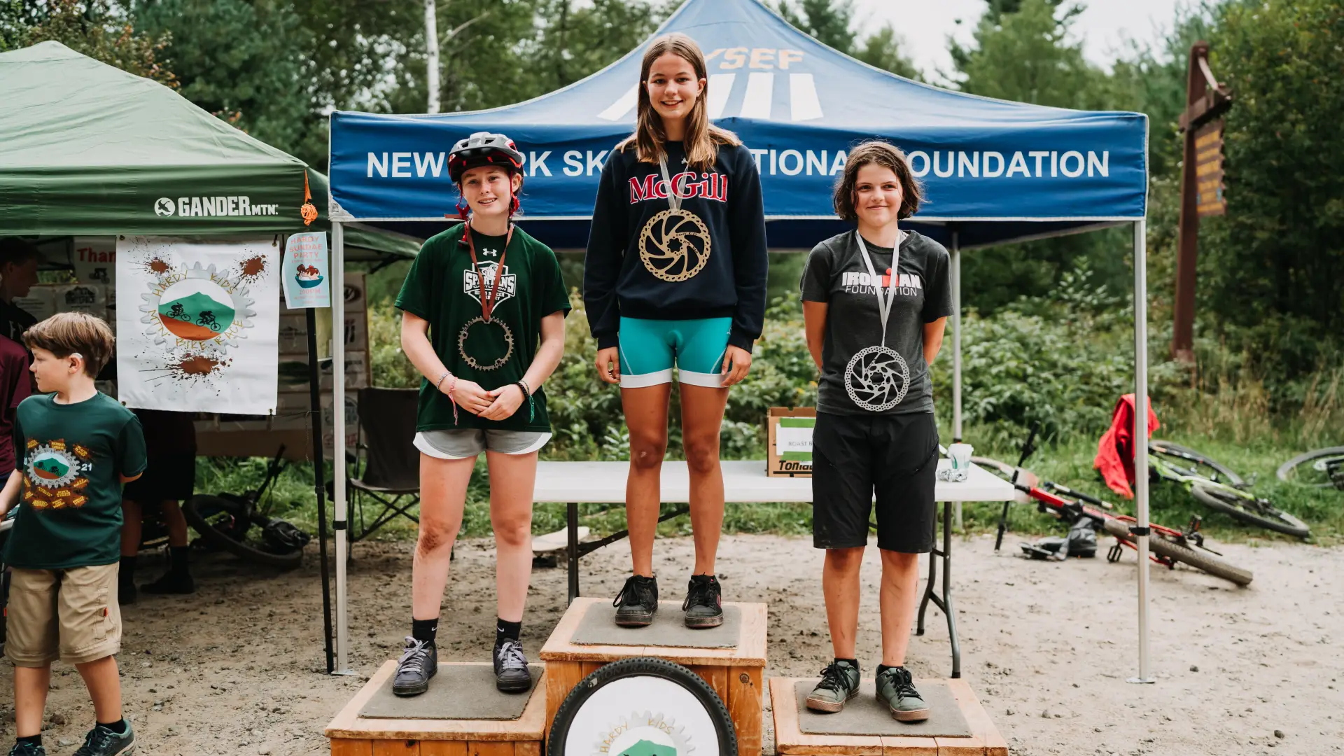 Three kids stand atop podium with medals at mountain biking event