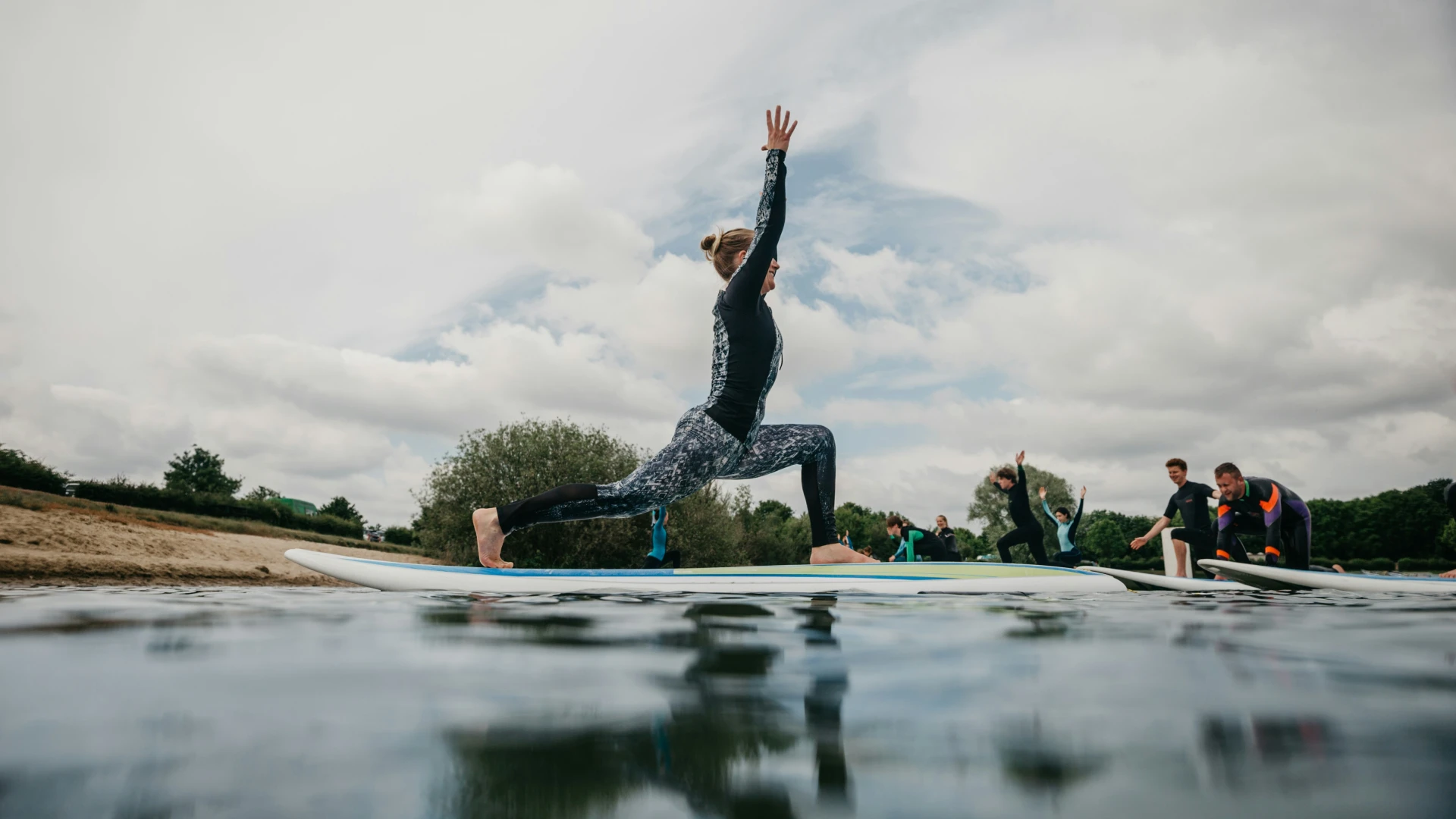 Stock image of person striking yoga pose on stand up paddle board on water with other paddlers mirroring