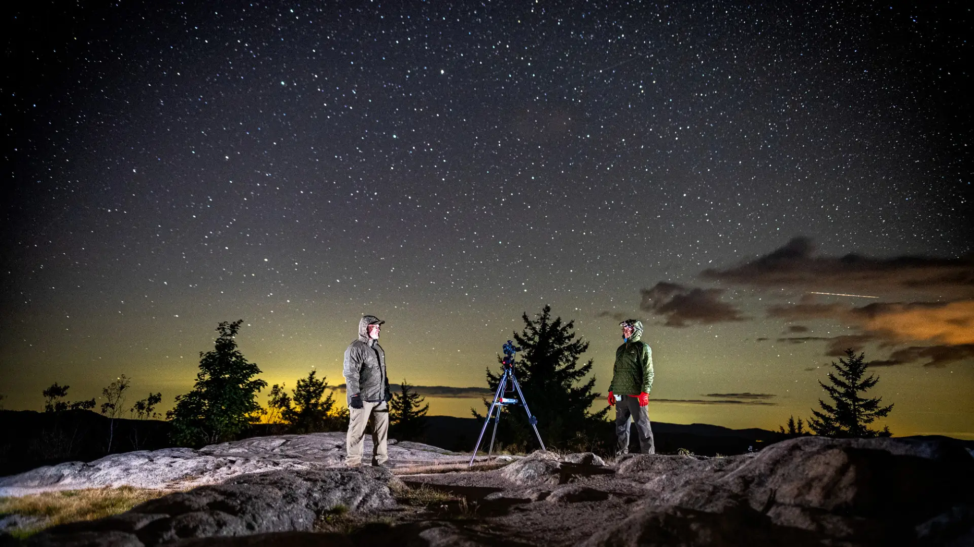 Two hikers photographing the night sky at the top of a summit.