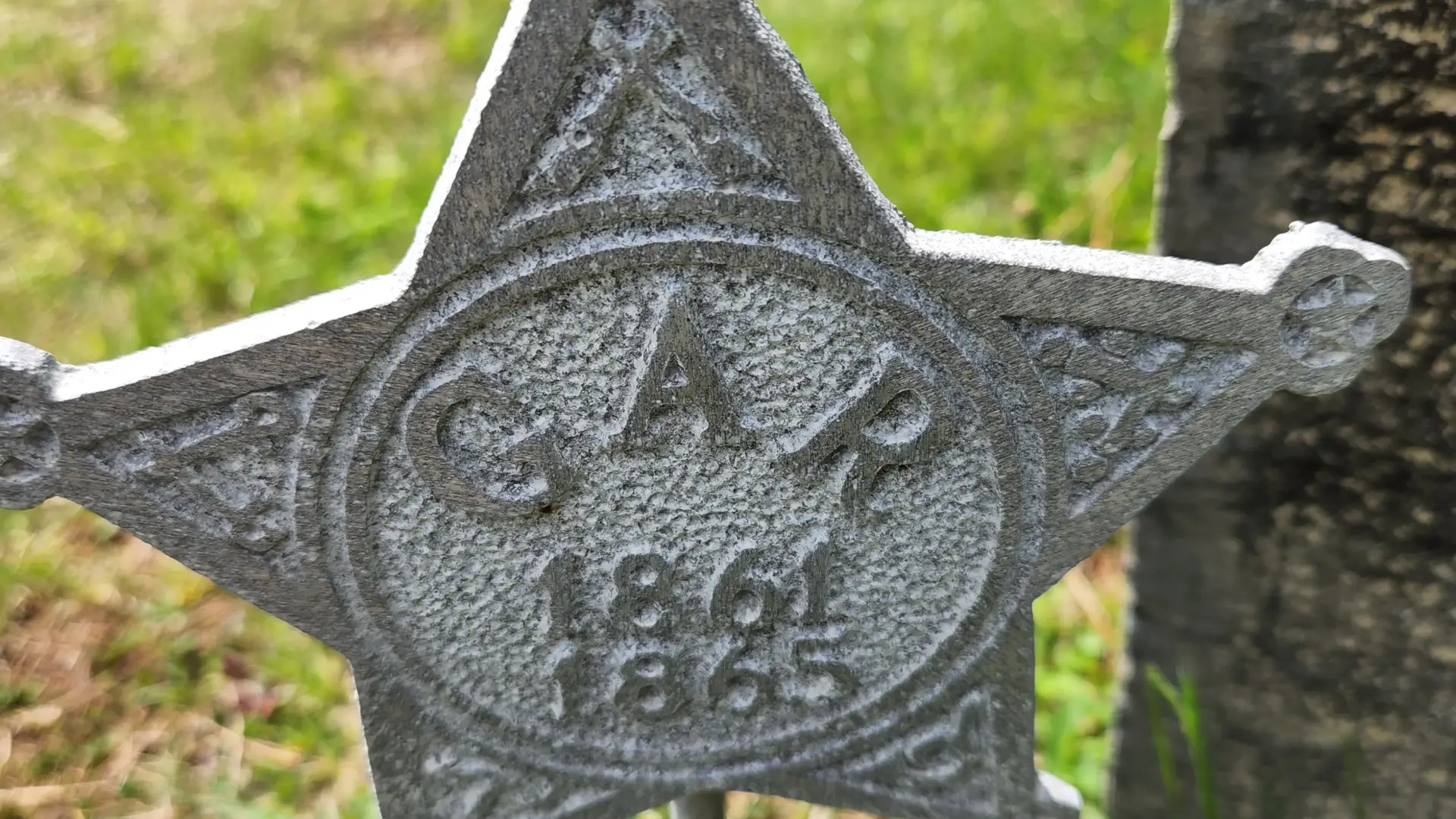 Close-up of a Grand Army of the Republic star placed on a grave in a grassy cemetery.