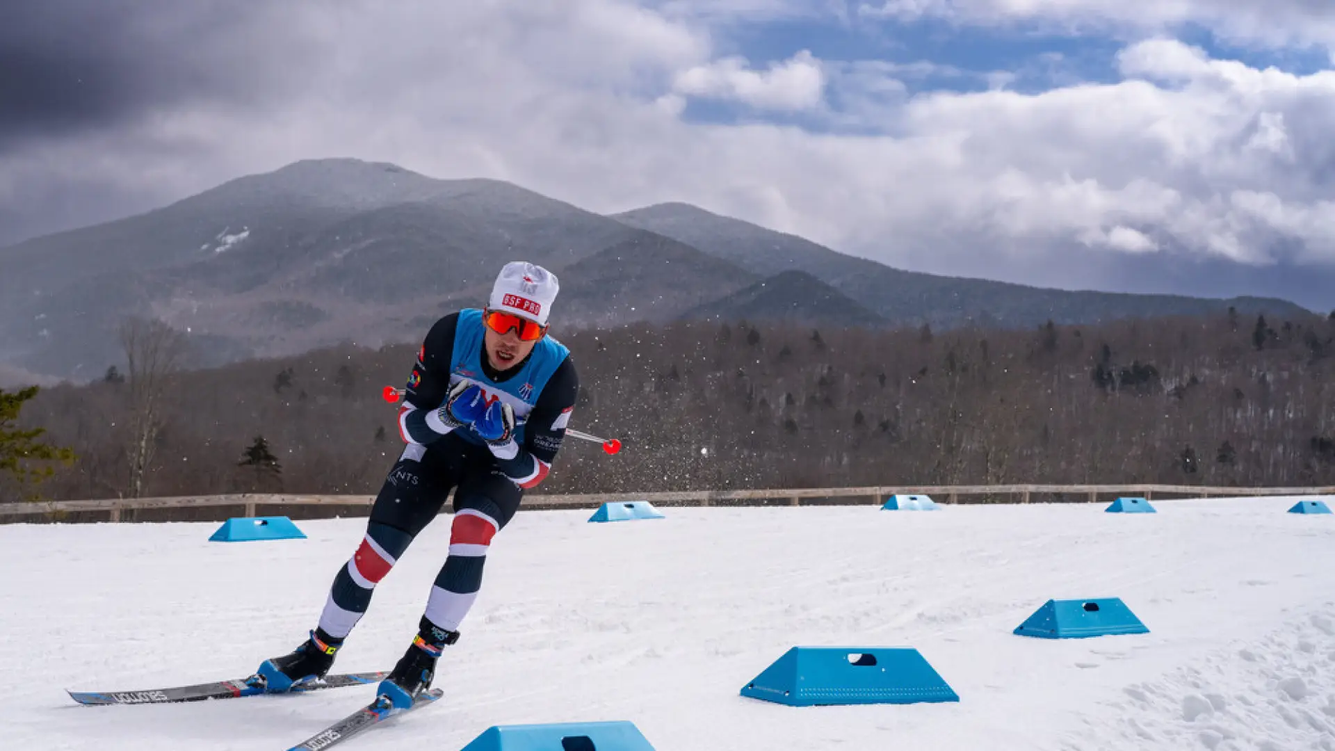 A skier in a blue and red outfit navigates a snowy course marked by blue obstacles. 