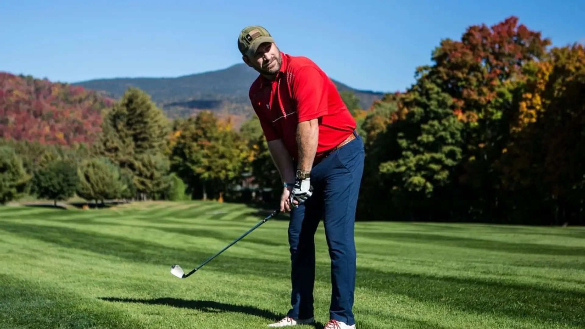 A man lines up his golf shot on a perfect green with the mountains behind