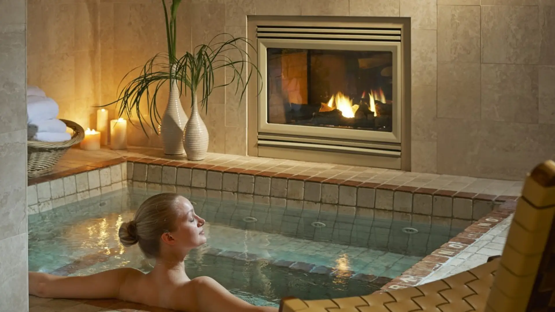 A woman relaxes in a private pool with fireplace and candles surrounding