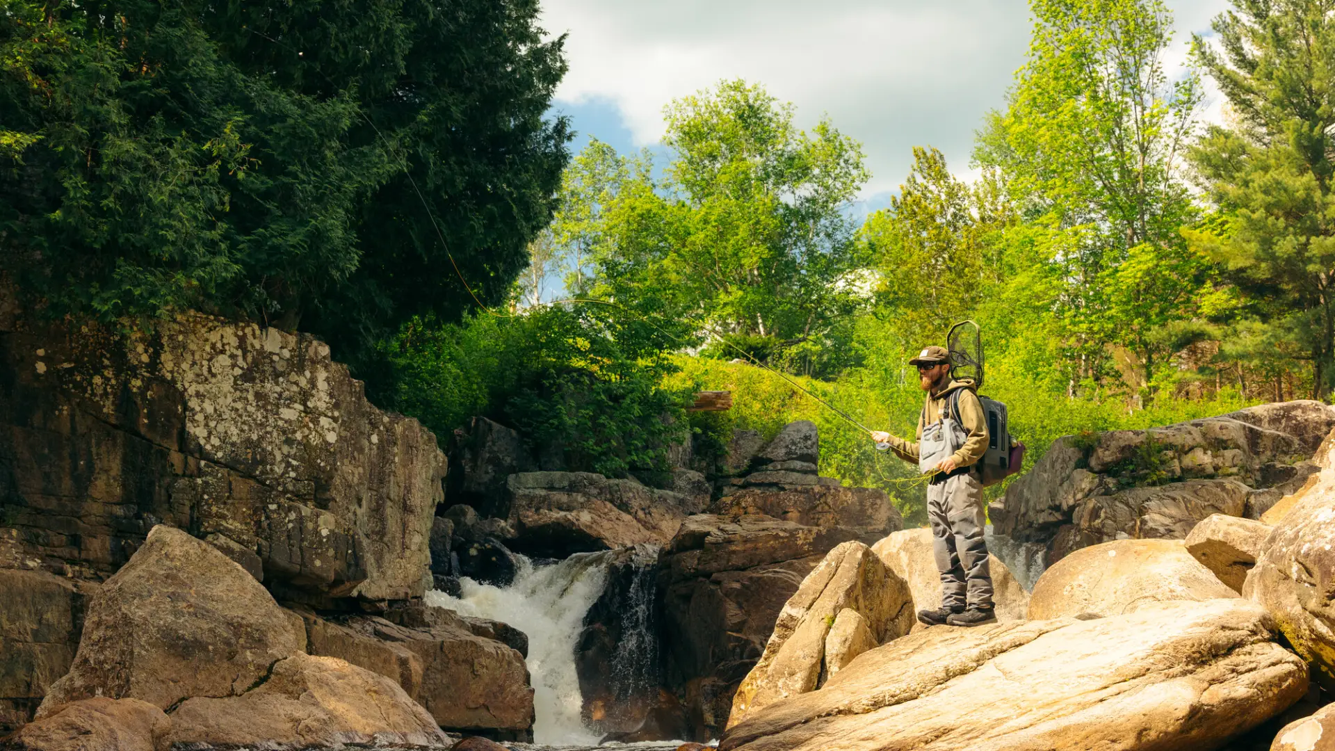 A flyfisher on some rocks by the water