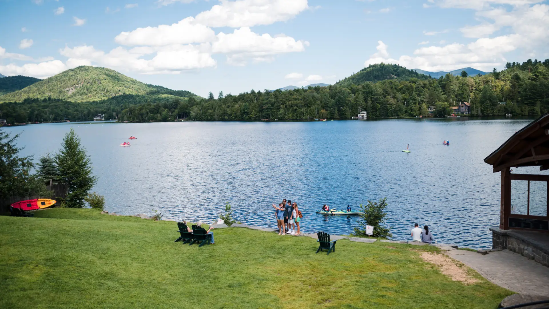 A sunny summer day at a green park with lake and mountains in the background.