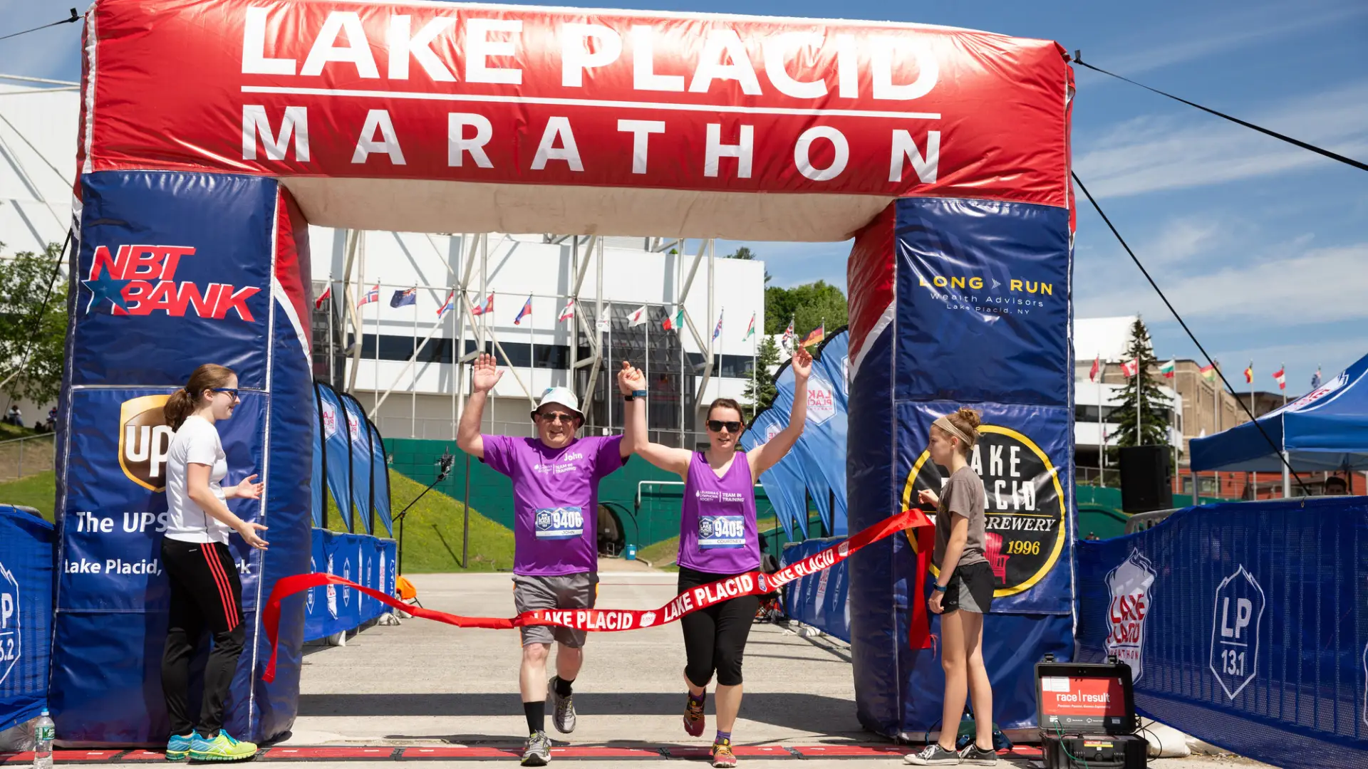 Two athletes cross the finish line holding hand in the air