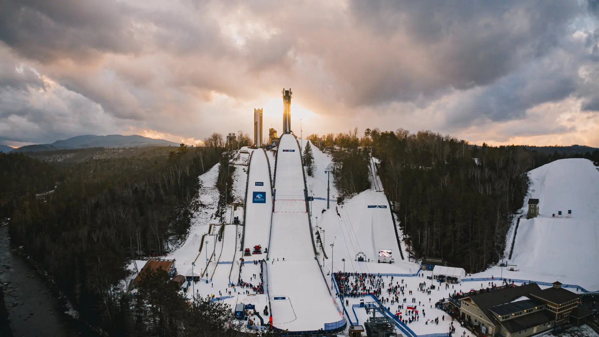 Straight on aerial shot of Lake Placid Ski Jumps in winter with sun setting behind the jump towers