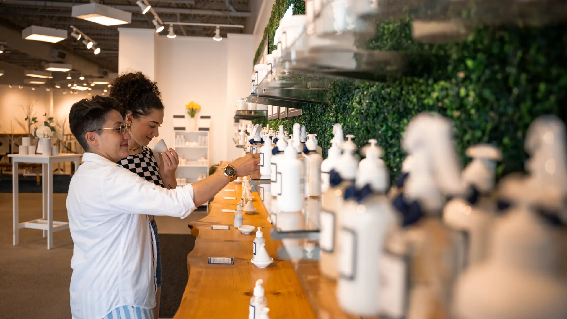 Two women look sample lotions at long counter of products