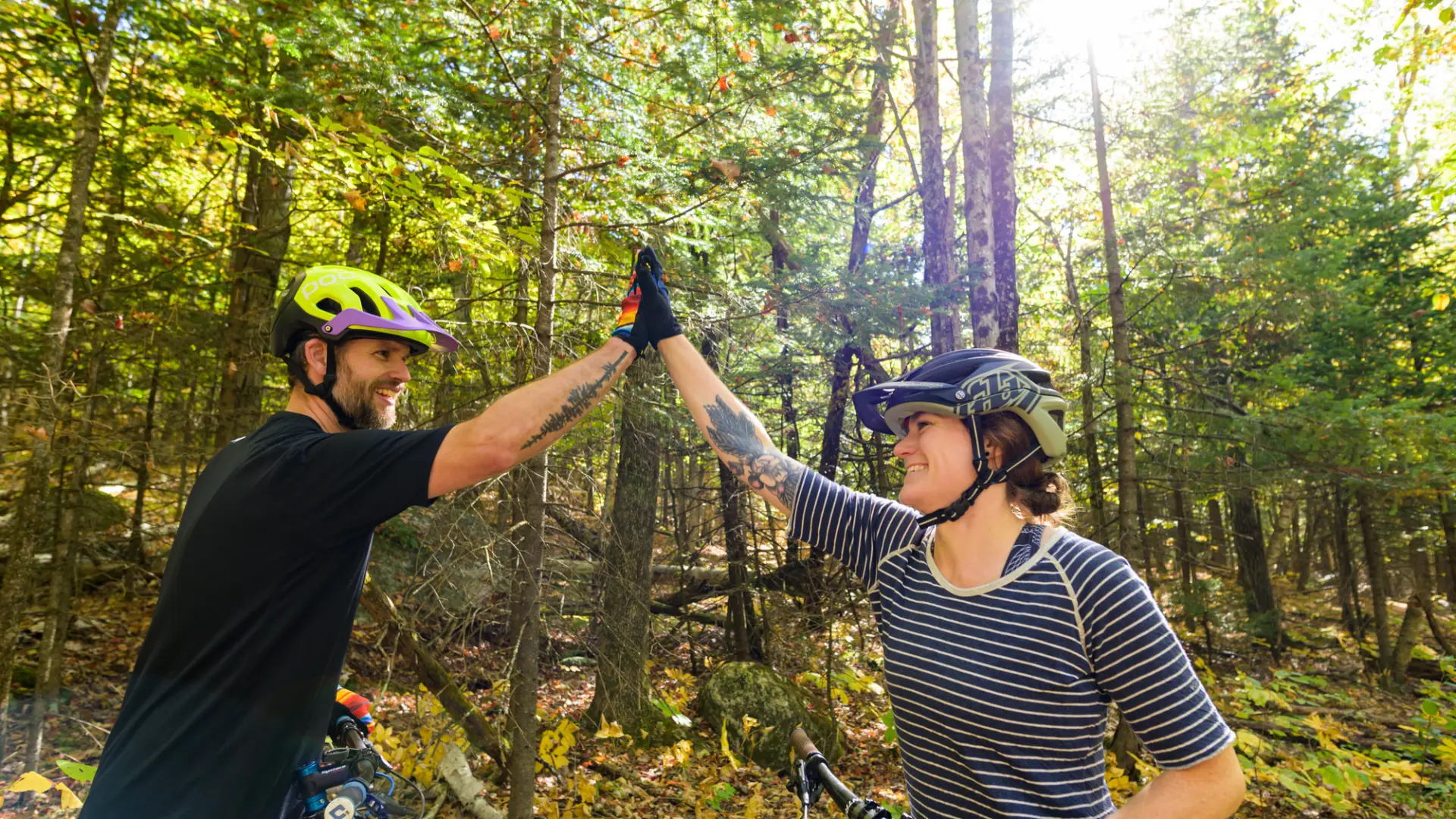 Two mountain bikers wearing biking gear stand on bikes high-fiving each other