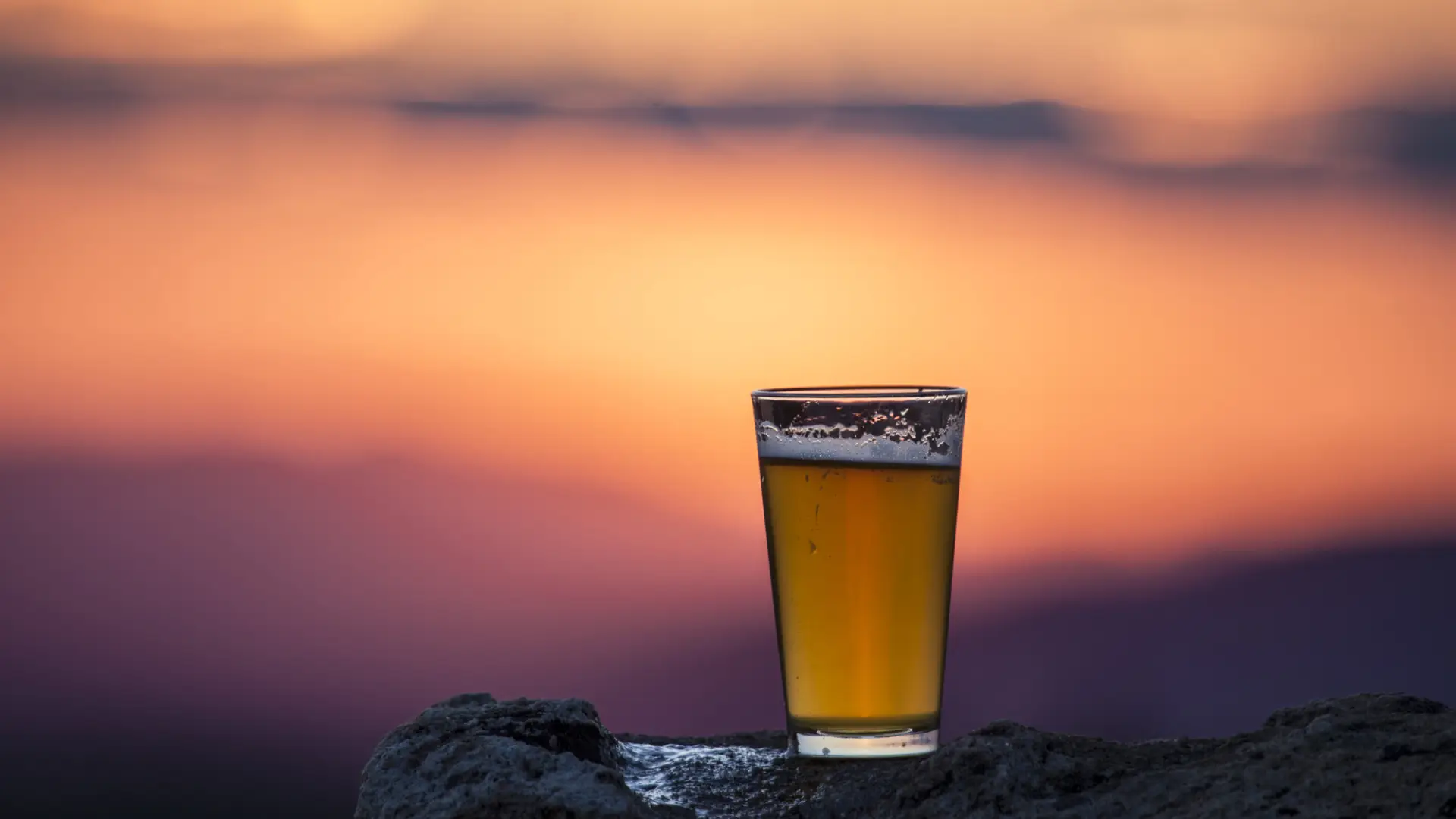 A cup of beer sits on a mountain top. 