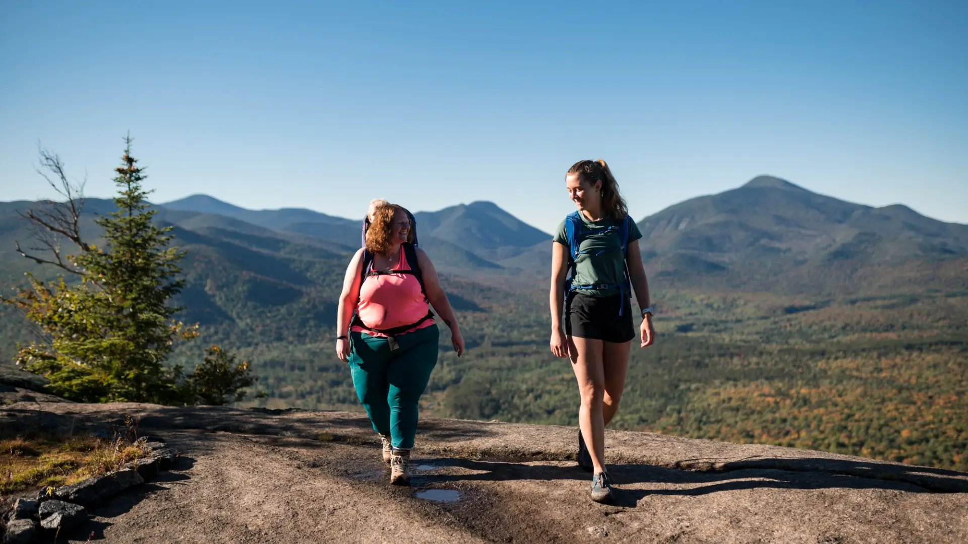 Two women hiking on a rocky mountain summit.