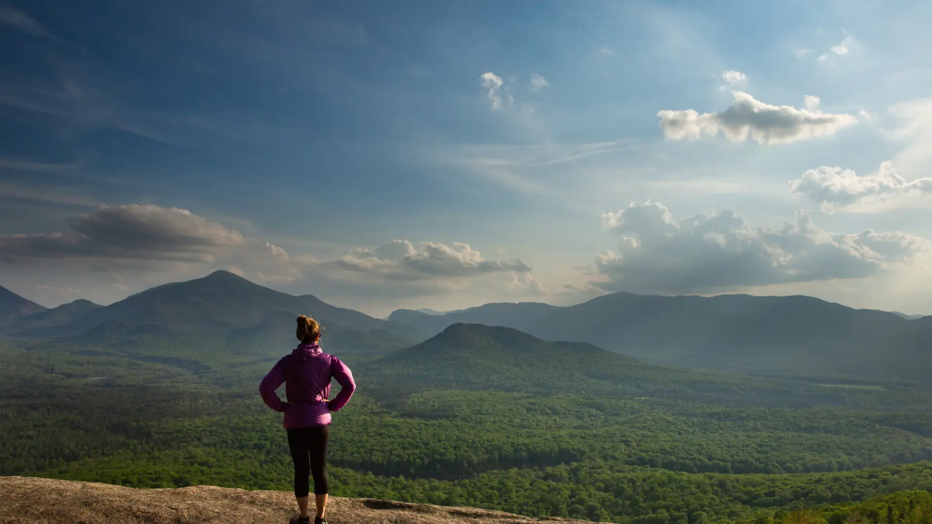 A hiker looks over the view at a mountain's summit