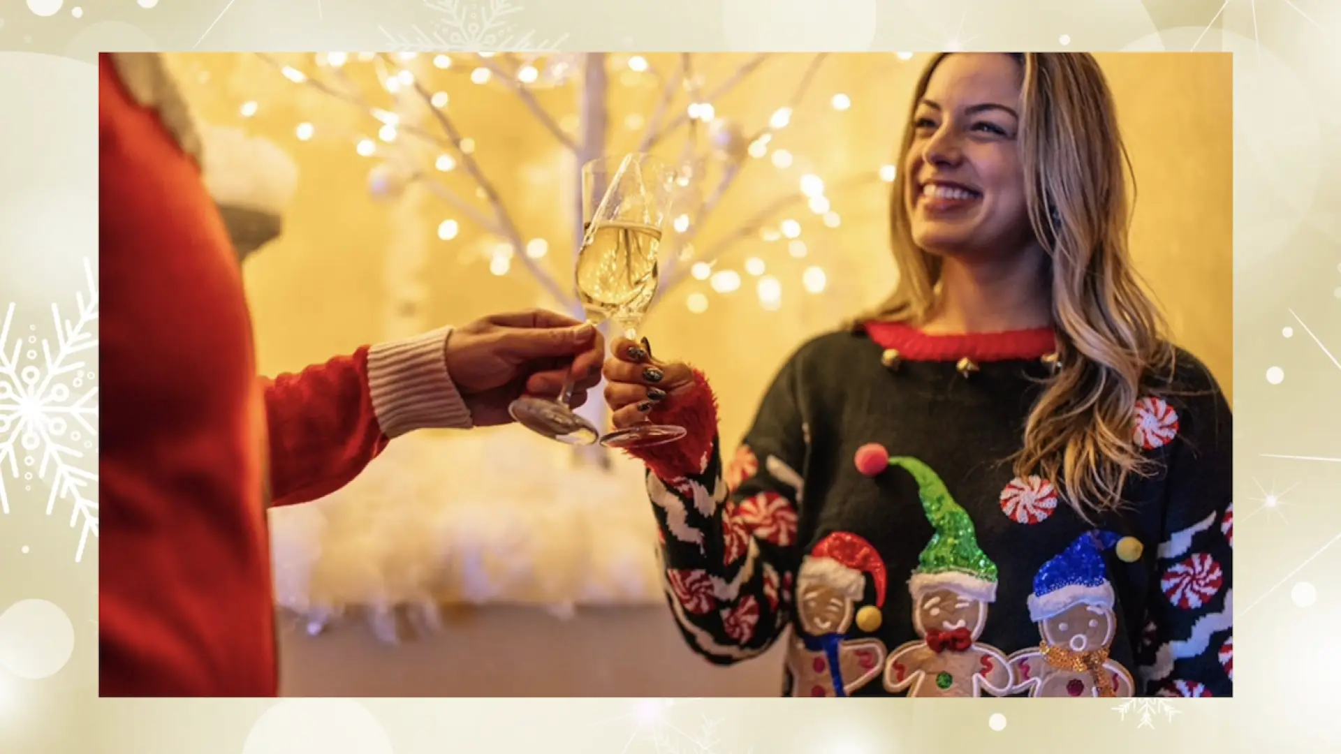 Woman in ugly holiday sweater toasts drink with person in a red sweater in front of gold, sparkling background