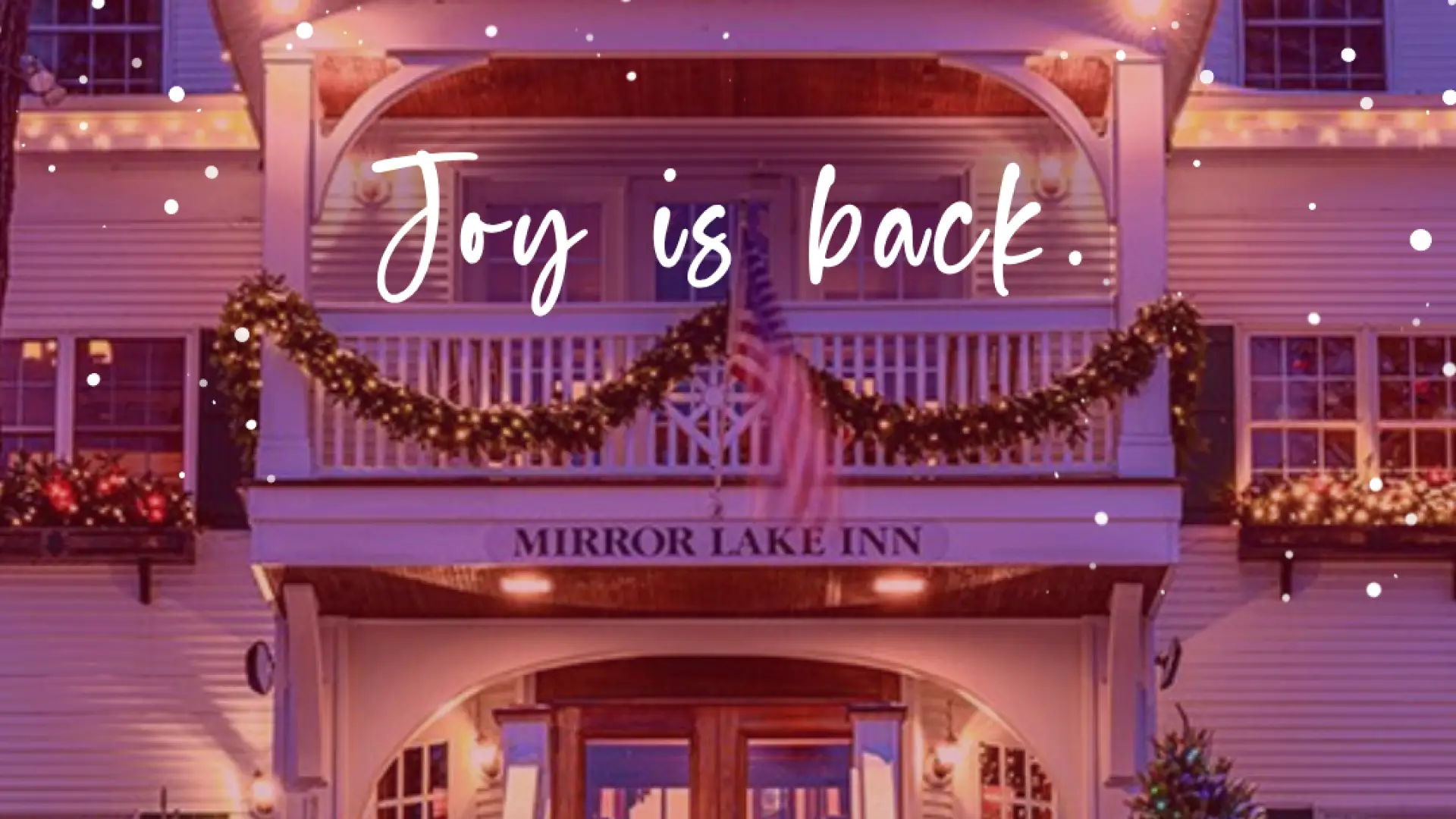 Festive inn entrance with twinkling lights and garlands. Snow falls gently. The text "Joy is back" overlays. Foreground: holly and berries. Cozy and cheerful.