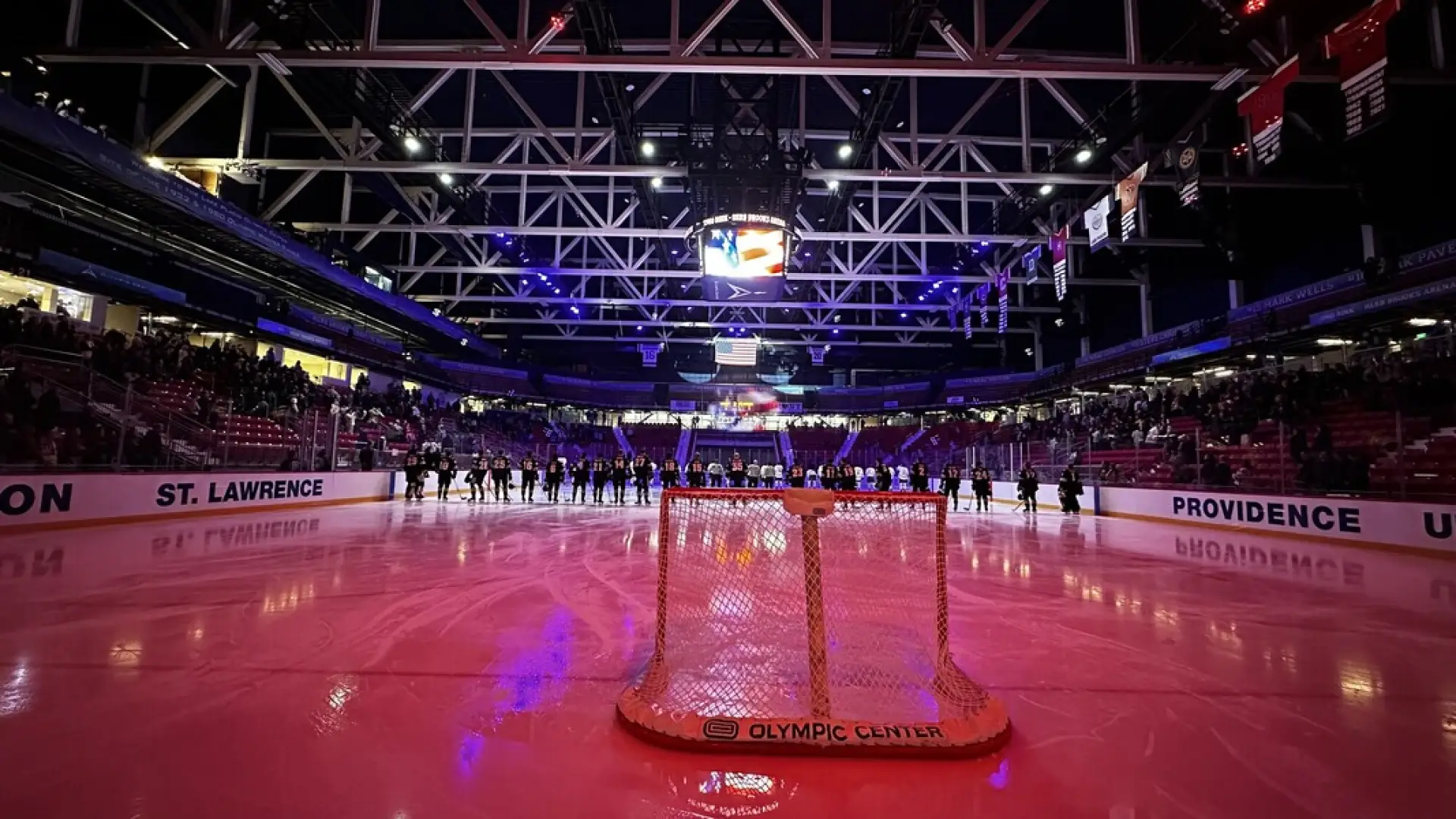 On-ice photo of hockey players lined up center ice with red lights illuminating the ice in the 1980 Herb Brooks Arena in Lake Placid