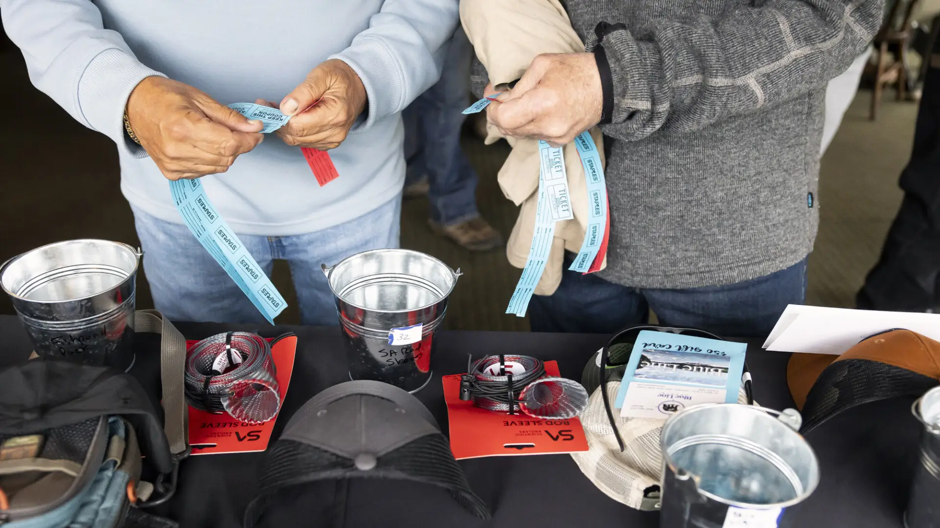 Two peoples' hands seen tearing raffle tickets at table of fly fishing raffle items at Two-Fly Challenge event