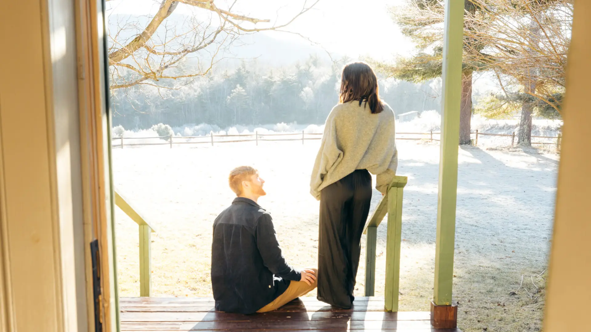 Couple on porch at misty morning, man sitting and woman standing leaning on rail