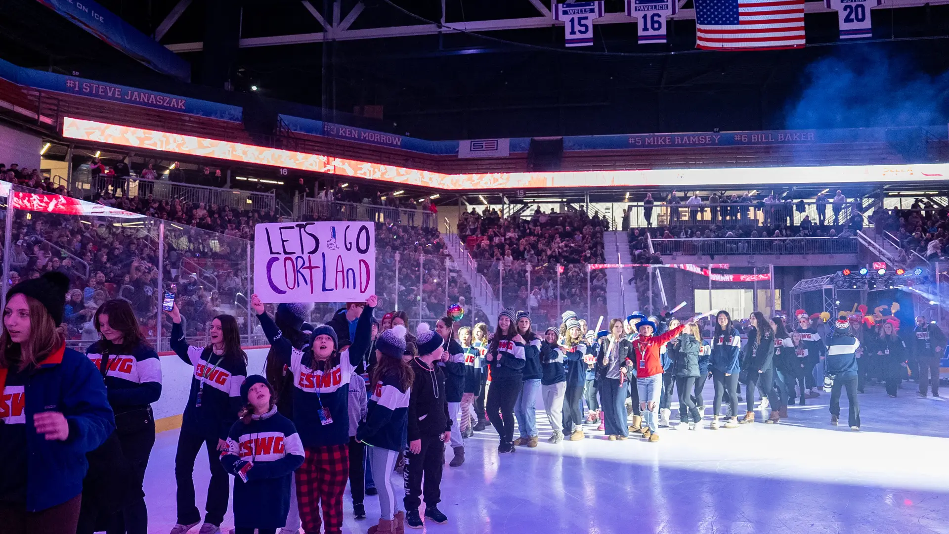 A large group of athletes wearing "ESWG" sweaters parades across the ice during an opening ceremony.
