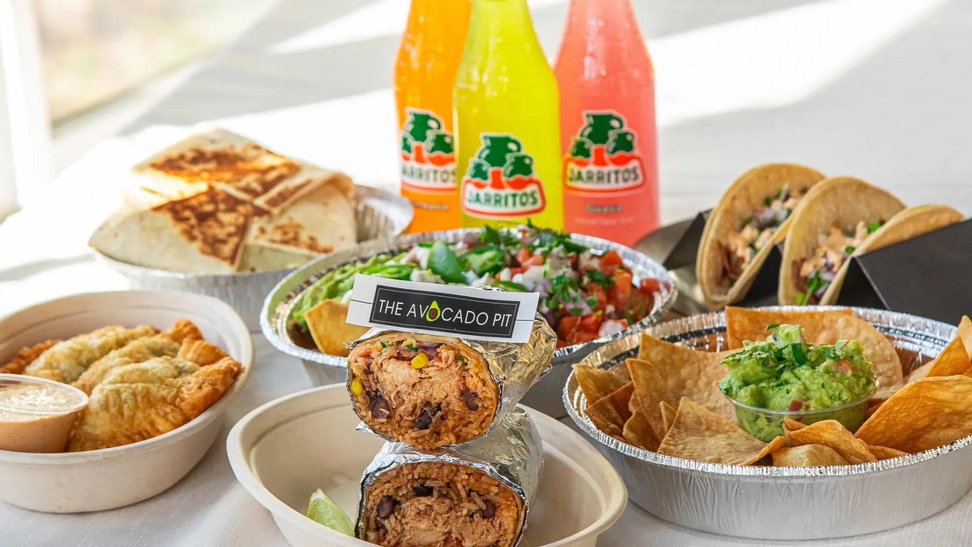 An assortment of bowls of nachos, burritos, tacos and Mexican flavors of sodas.