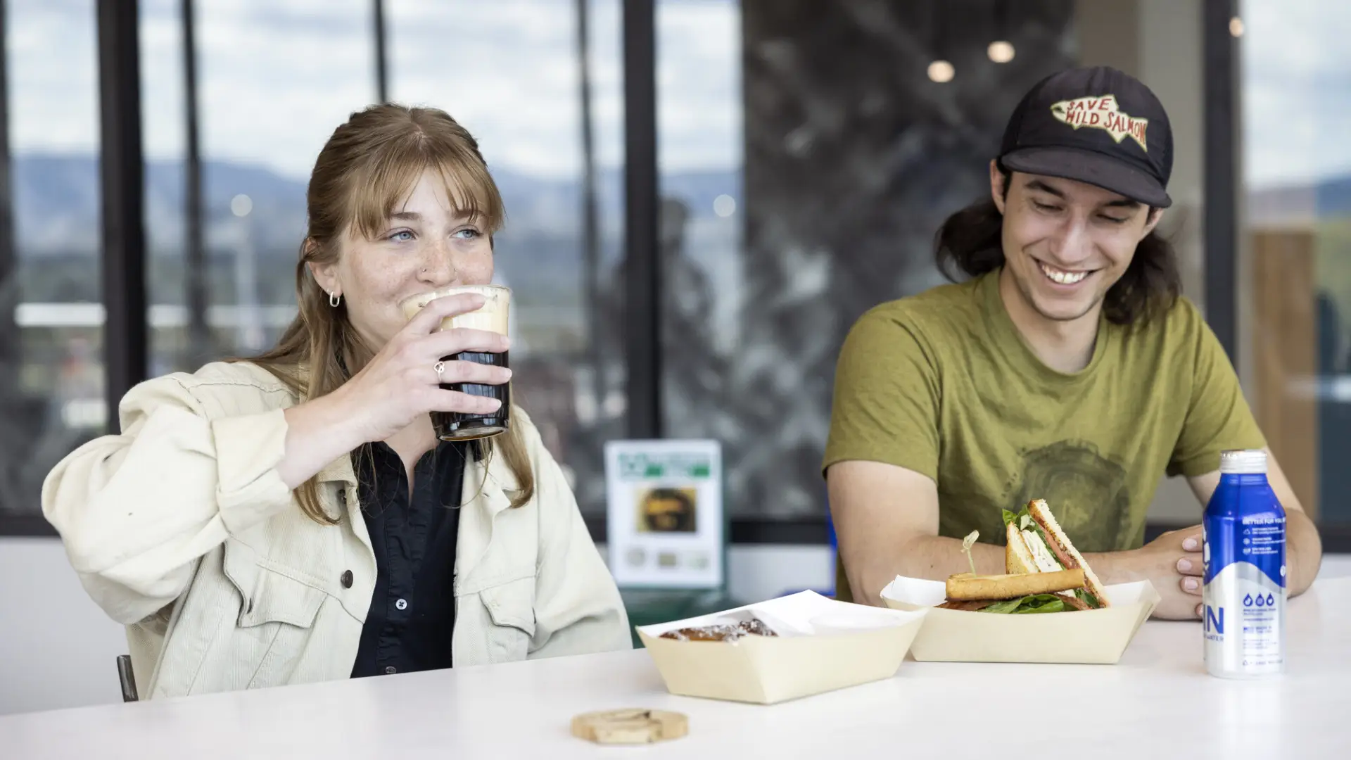 A man and woman enjoy coffee and sandwiches on a deck.