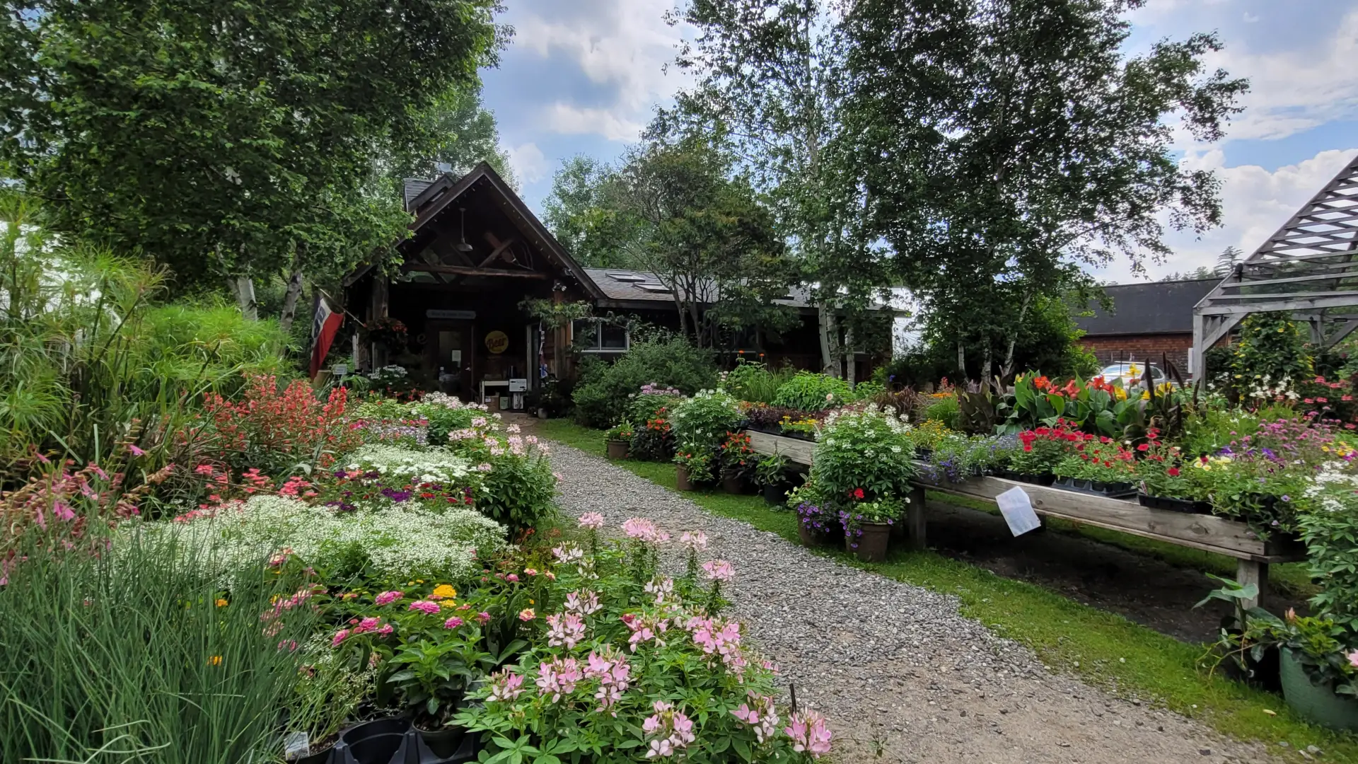 The exterior of East Branch Organics in Keene NY with lots of flowers and a wooden building at the end of a stone path