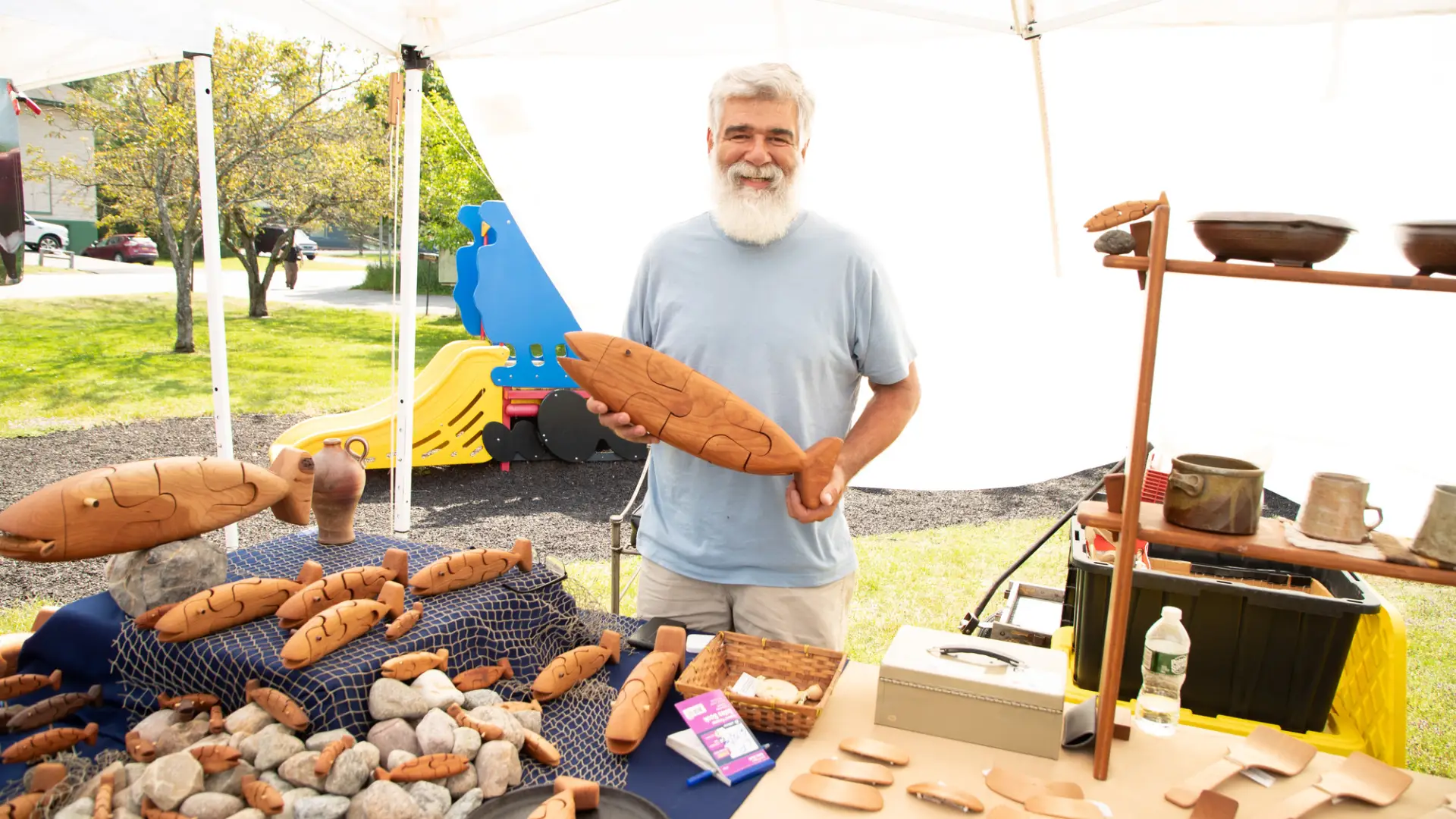 A local craftsman holds up a wooden fish at the farmers market.
