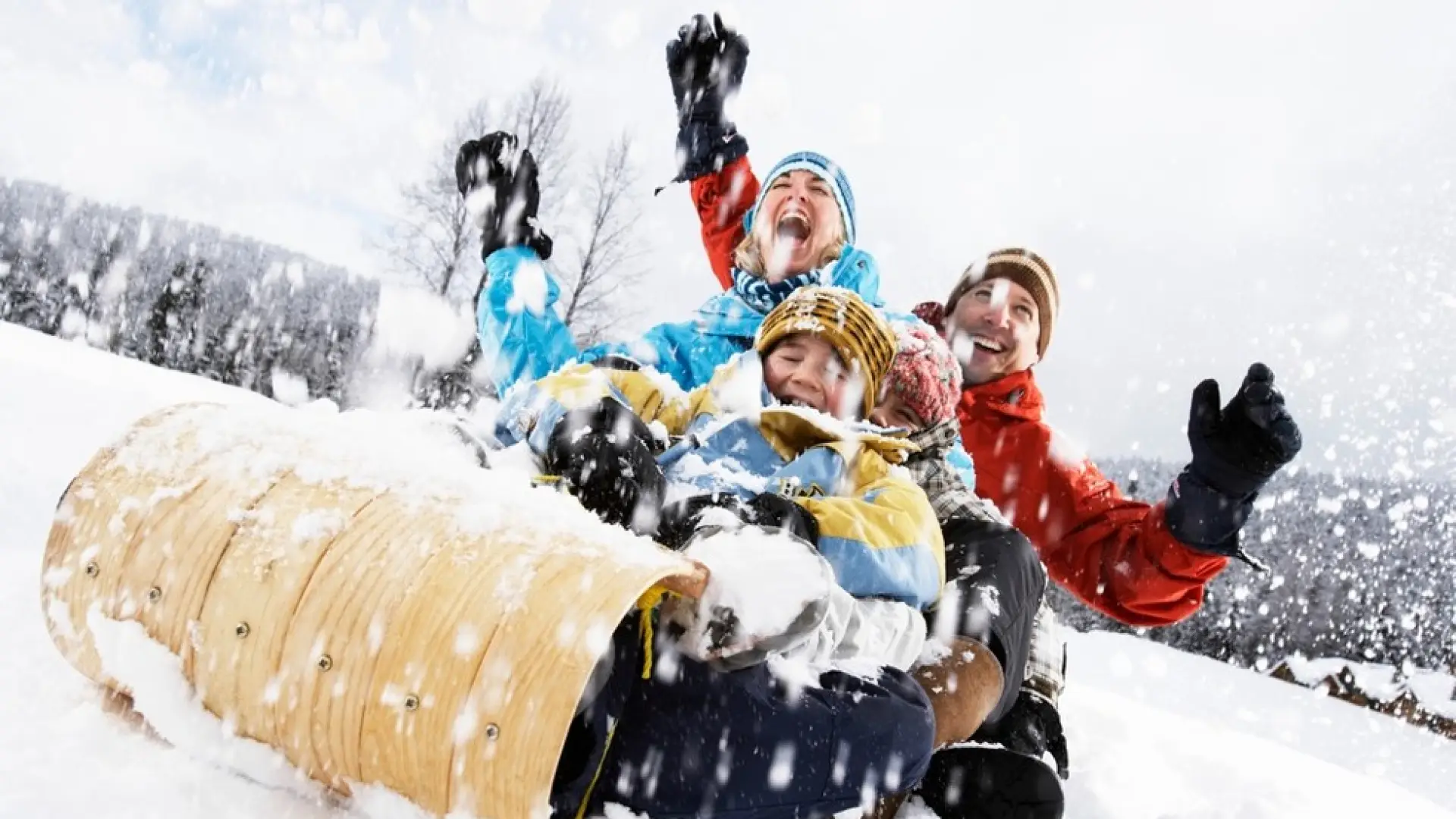 A young family  laughs their way down the sledding hill on a tobogan as the snow flies around them