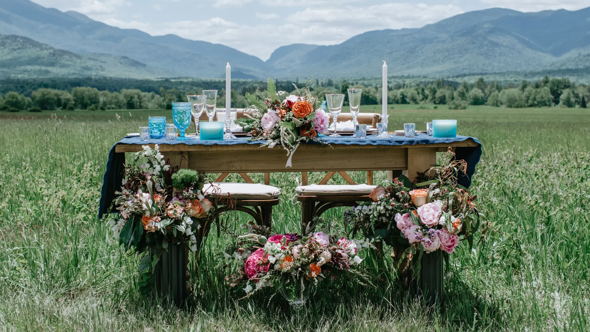 The Sweetheart table adorned with flowers, candles and blue glass in a meadow with the high peaks mountains in the background