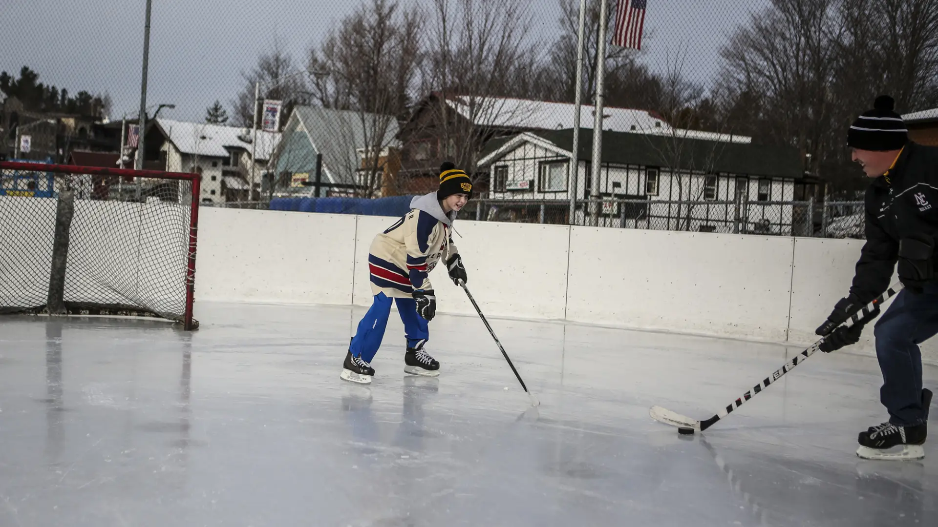 A father and son play hockey at a small rink