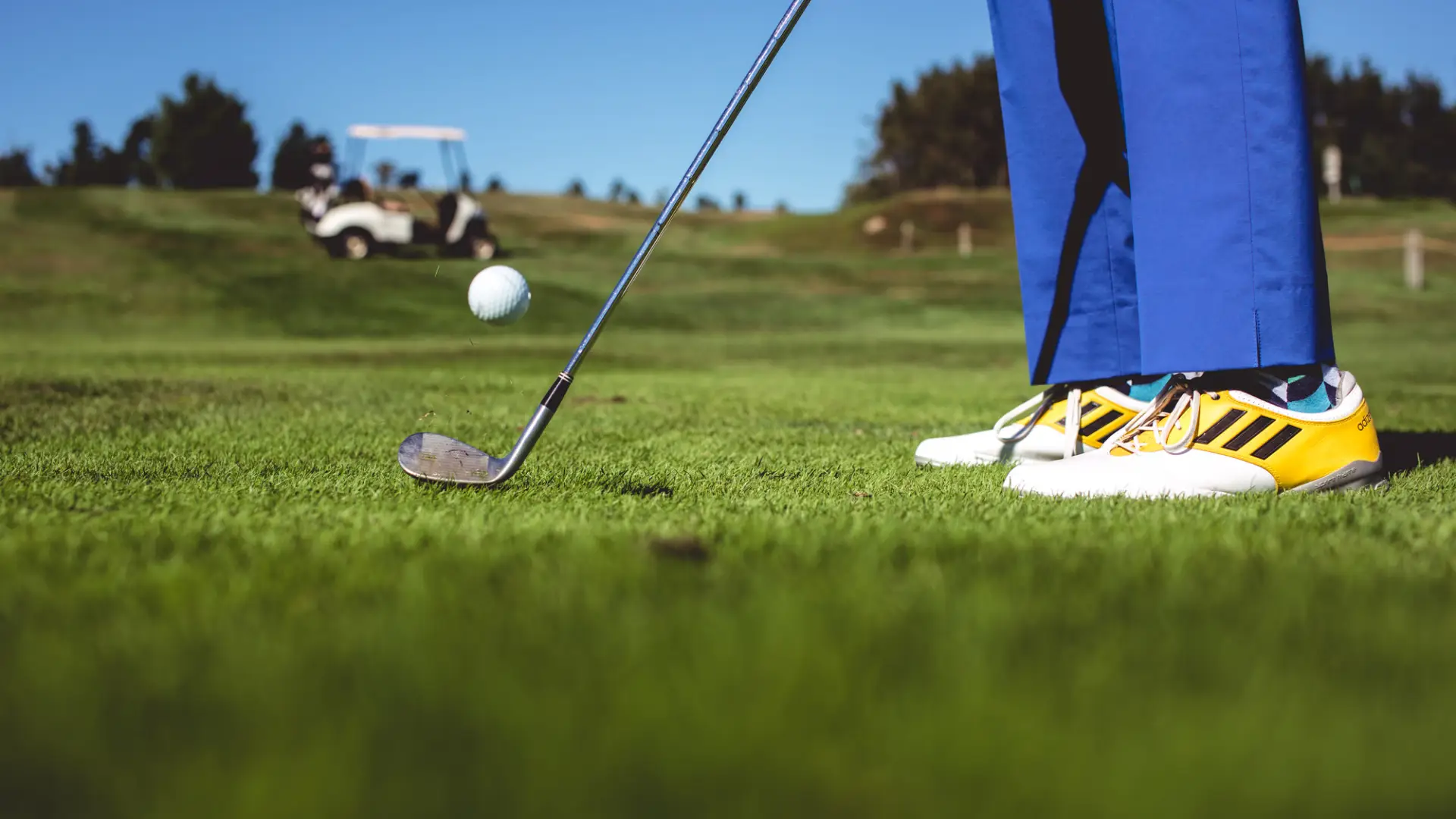 Close-up of a golfer's feet as he strikes the ball with cart in background.