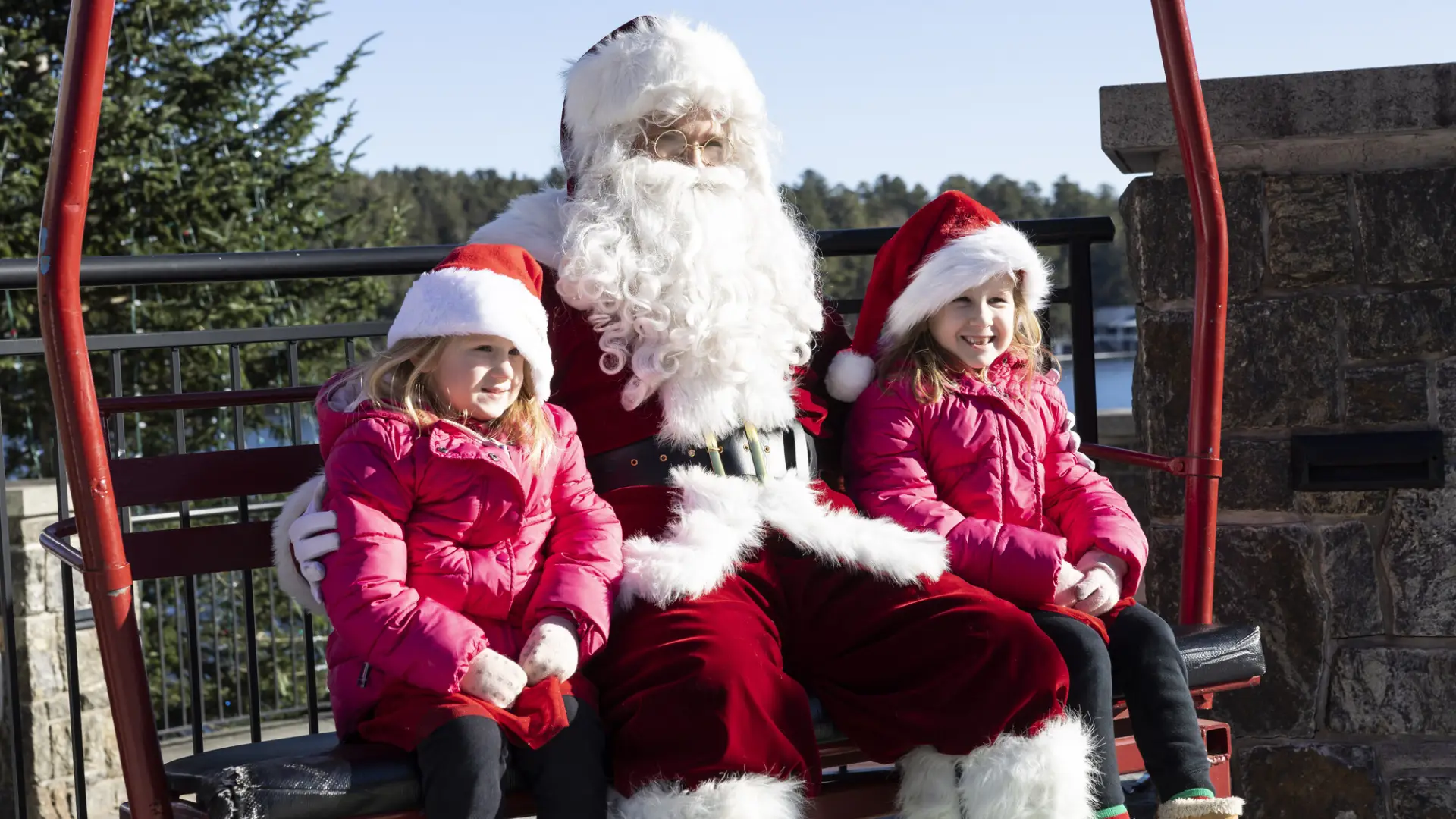 A couple of children having their picture taken while sitting next to Santa.
