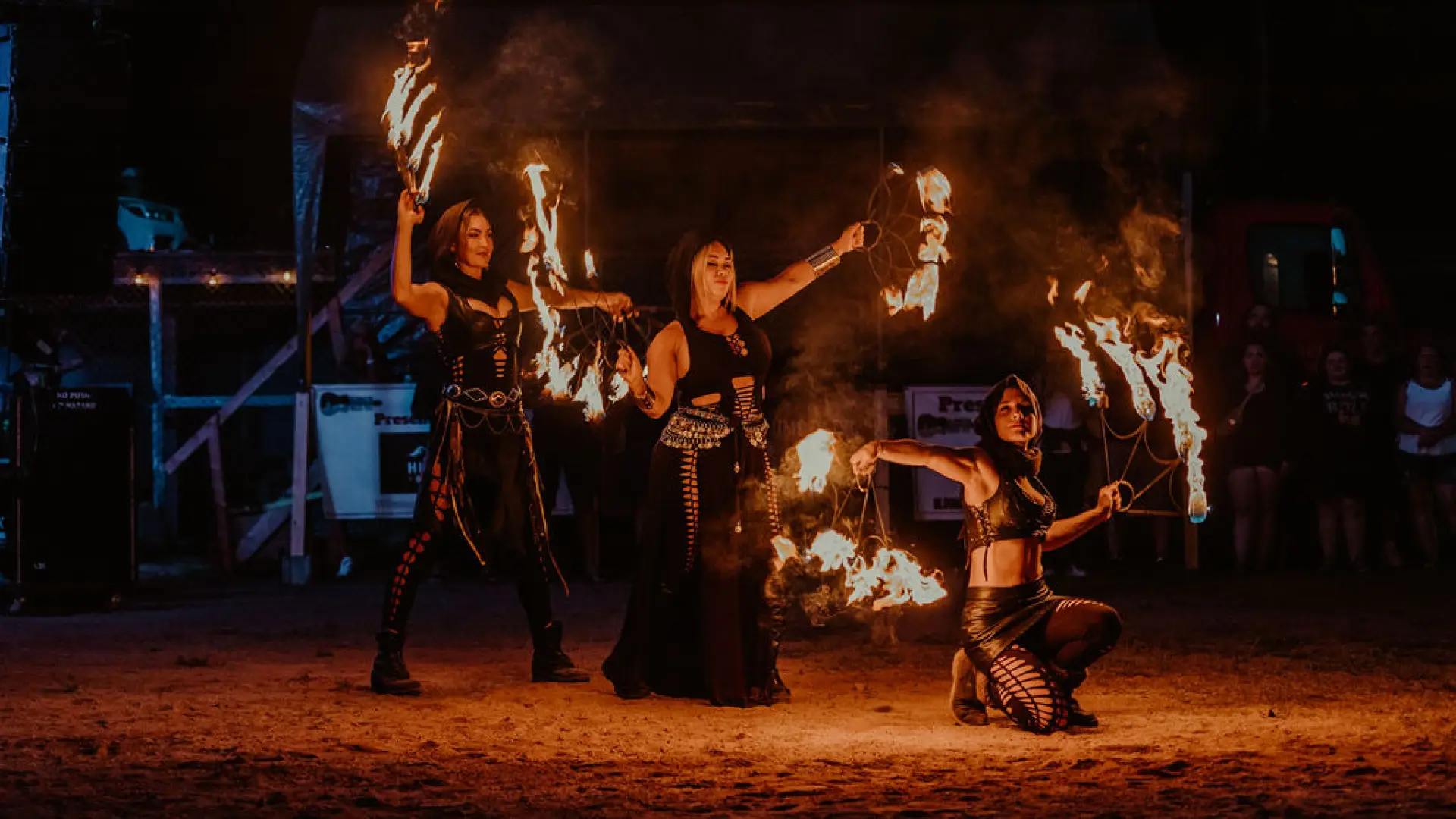 Trio of fire dancers seen with lighted torches posing in dark outdoor venue