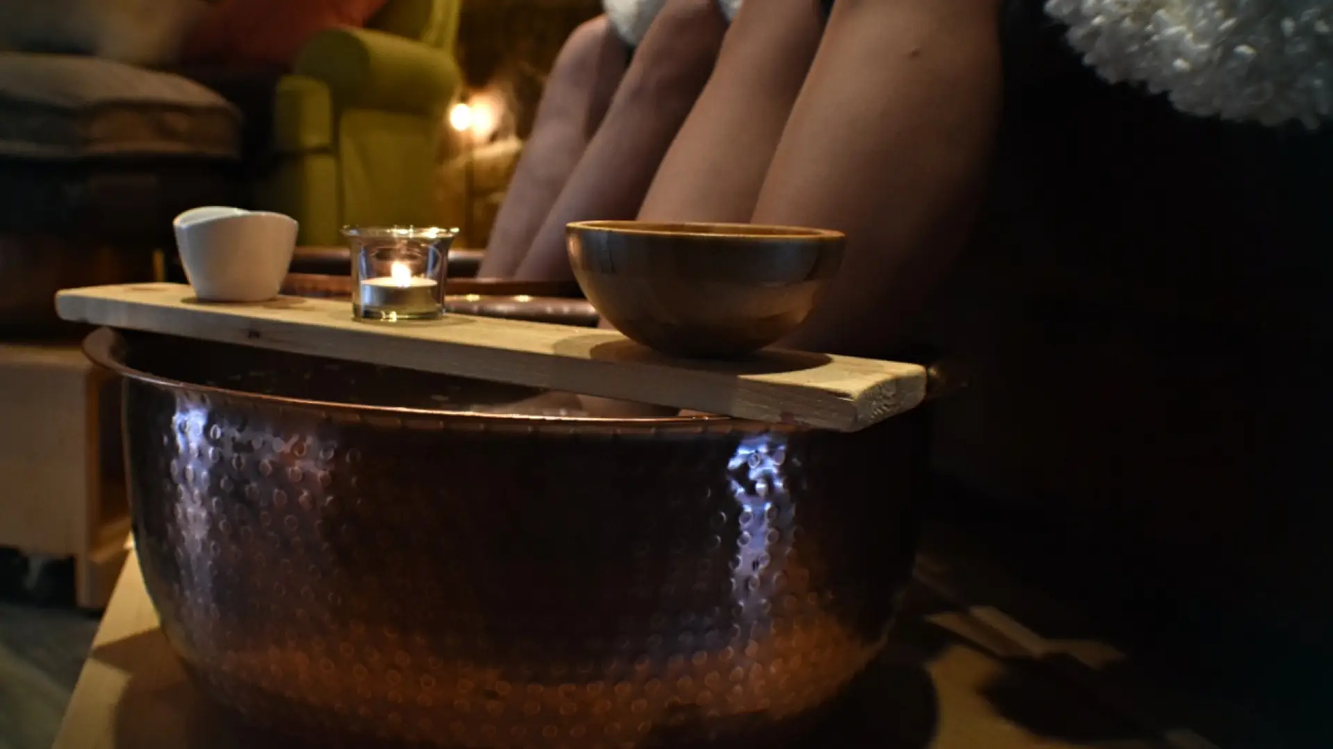 Two people sit with their feet in hammered copper bowls for a foot treatment.