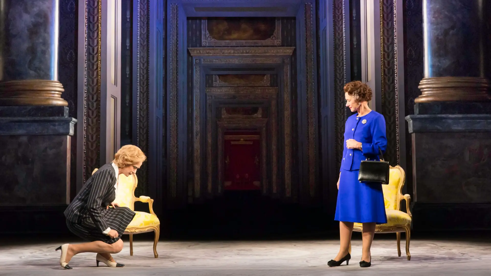 Two women dressed in professional mid-century attire face each other on a stage set featuring a long corridor of doorways.