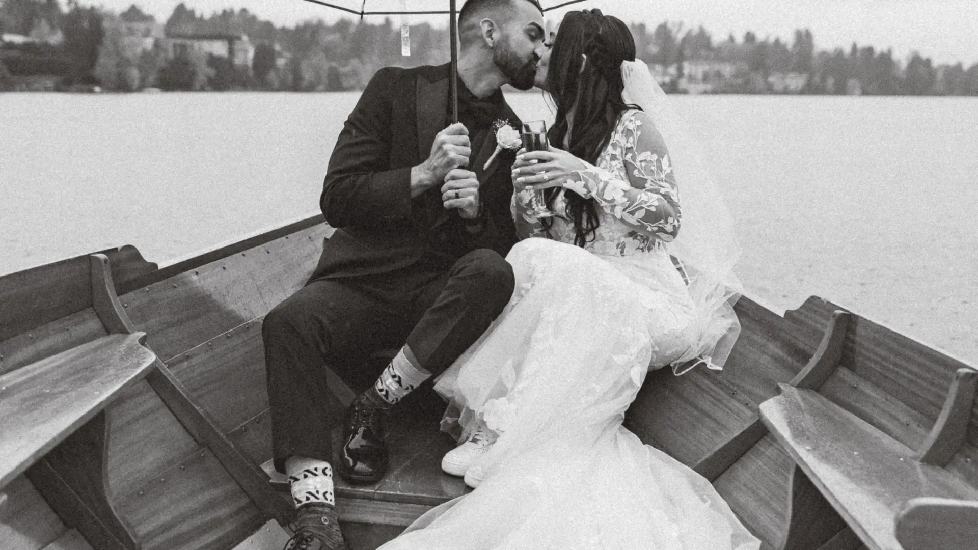 Black and white photo of the bride and groom kissing under an umbrella in the rain
