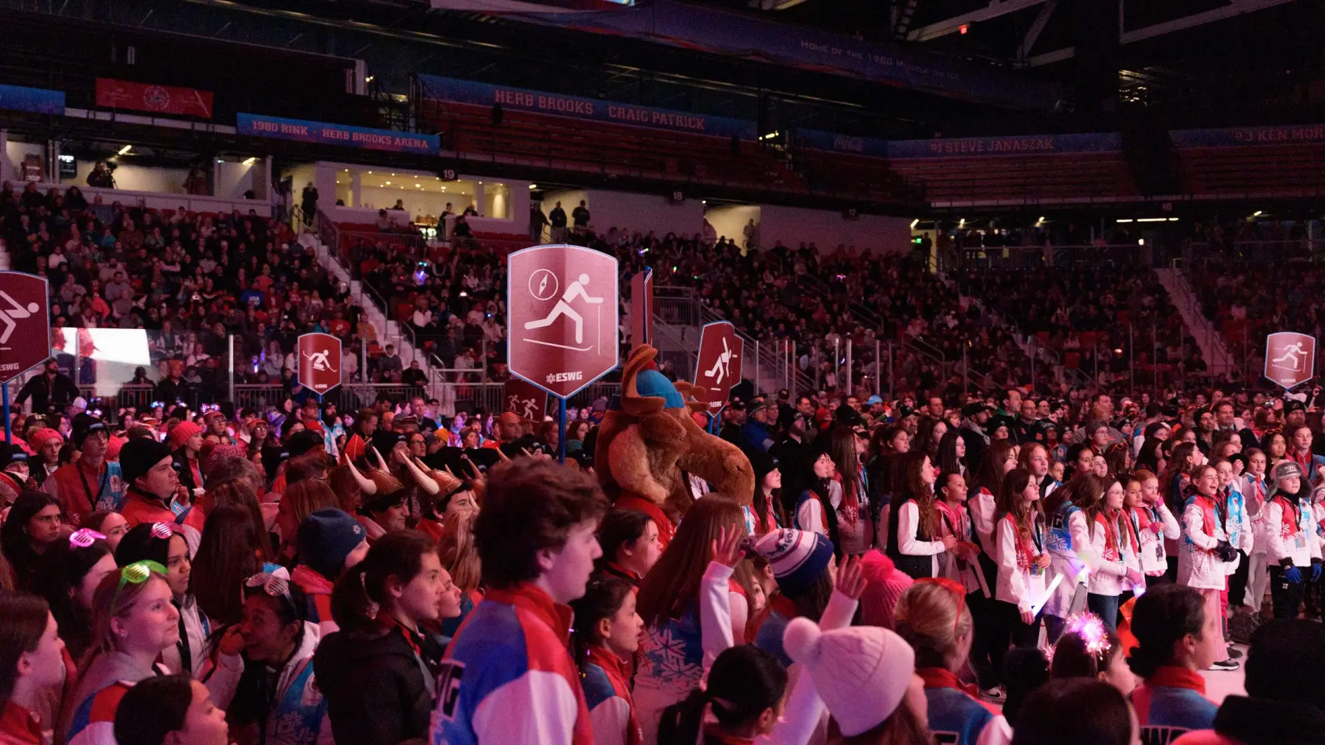 A large crowd fills an indoor arena, watching the Empire State Winter Games Opening Ceremony.  The atmosphere is vibrant and energetic.