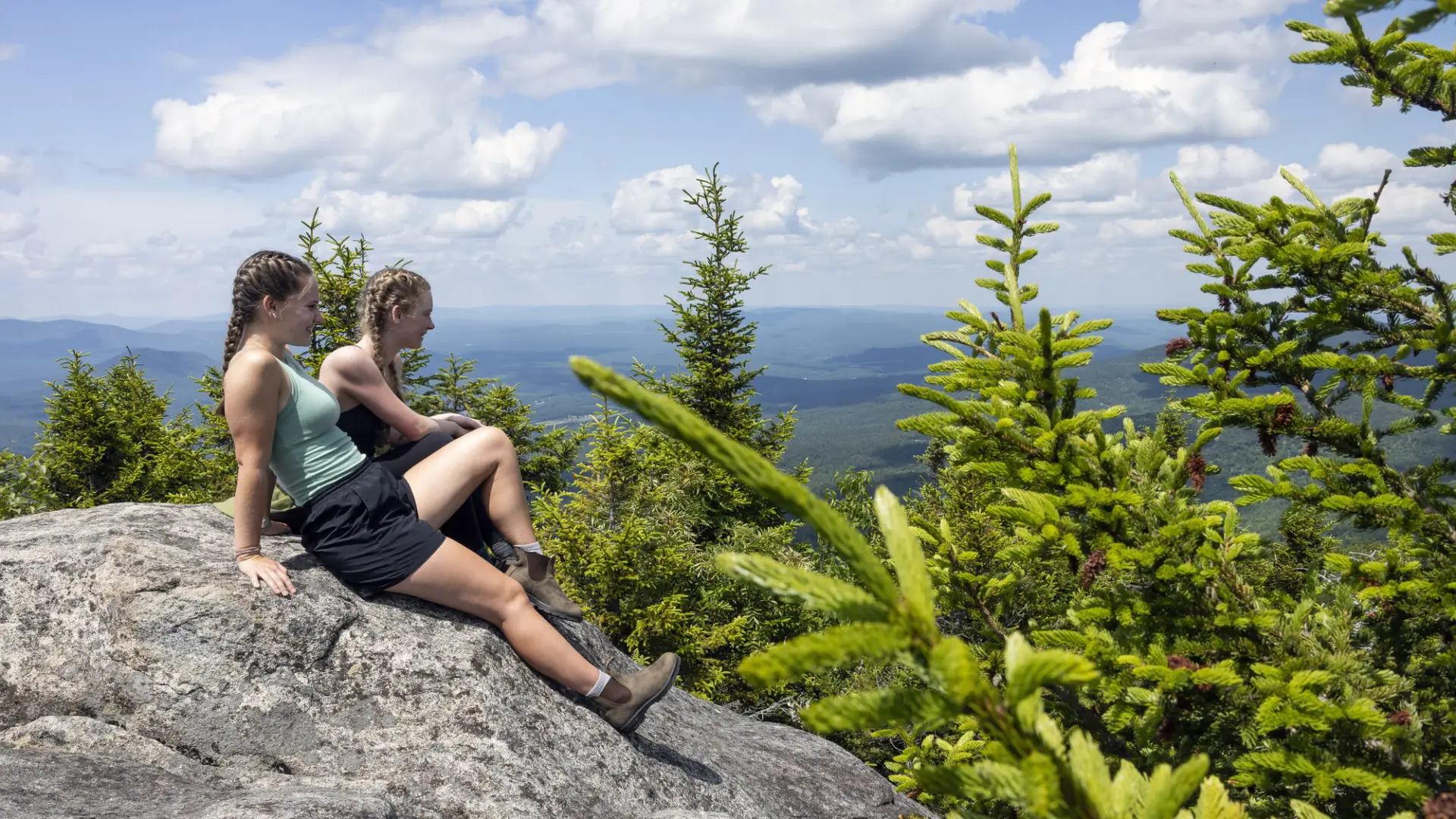 Two young women sit on a rocky summit.
