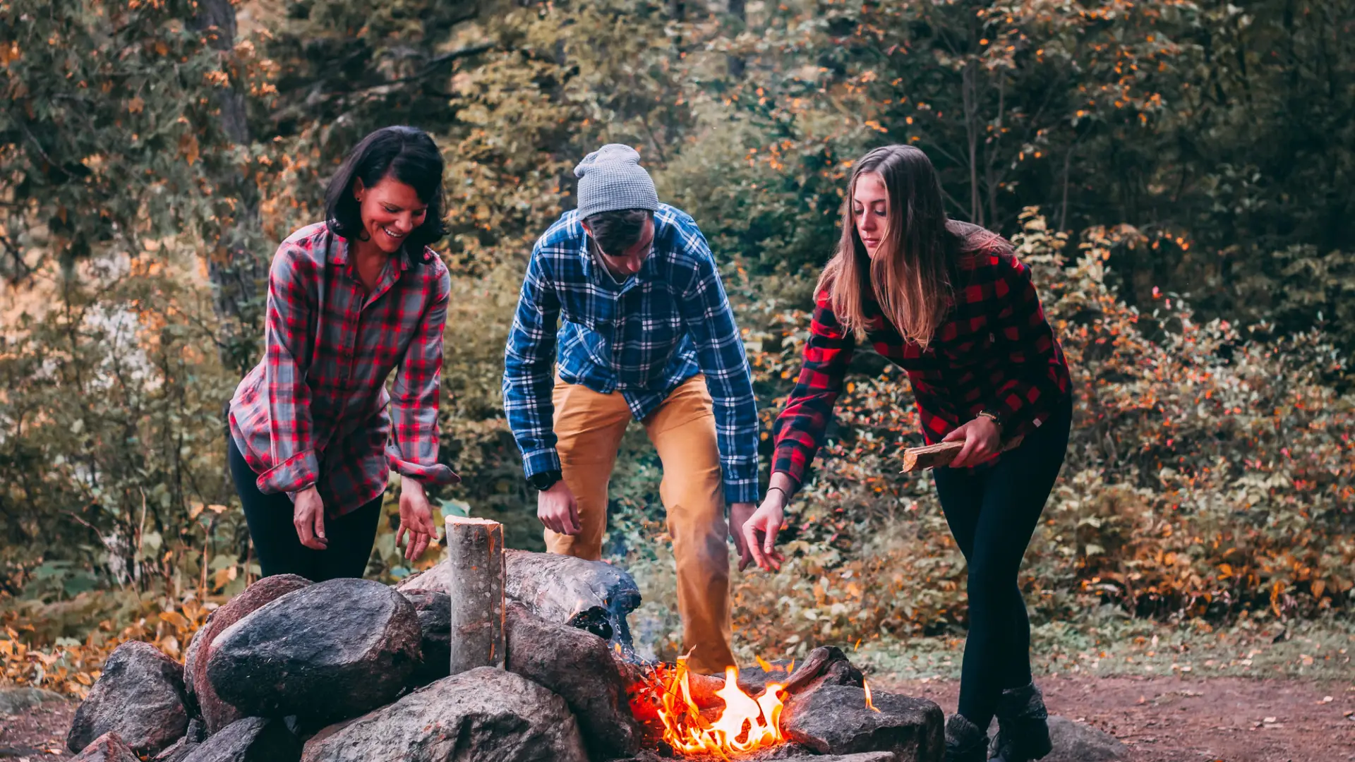 Three people tend to a fire. 