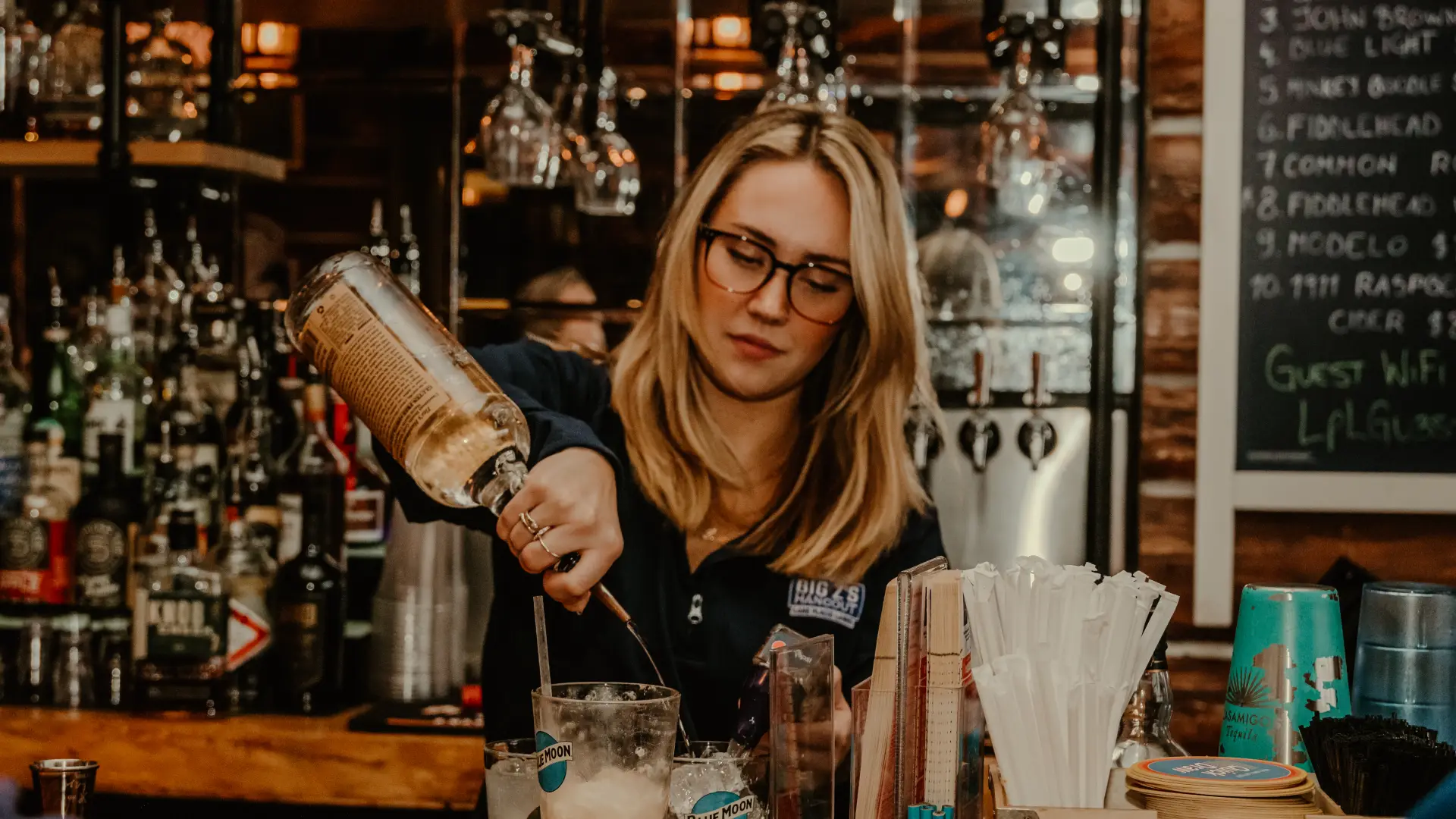 A smiling bar tender makes a cocktail with the full bar at Big Zs.  Photo Credit to A. Kelly.