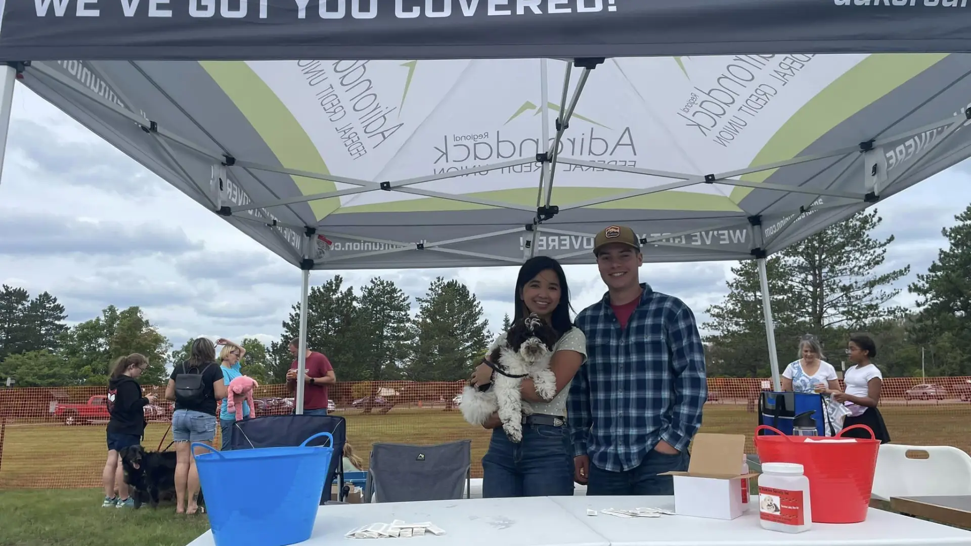 A couple holds a dog in a vendor tent at Bark in the Park