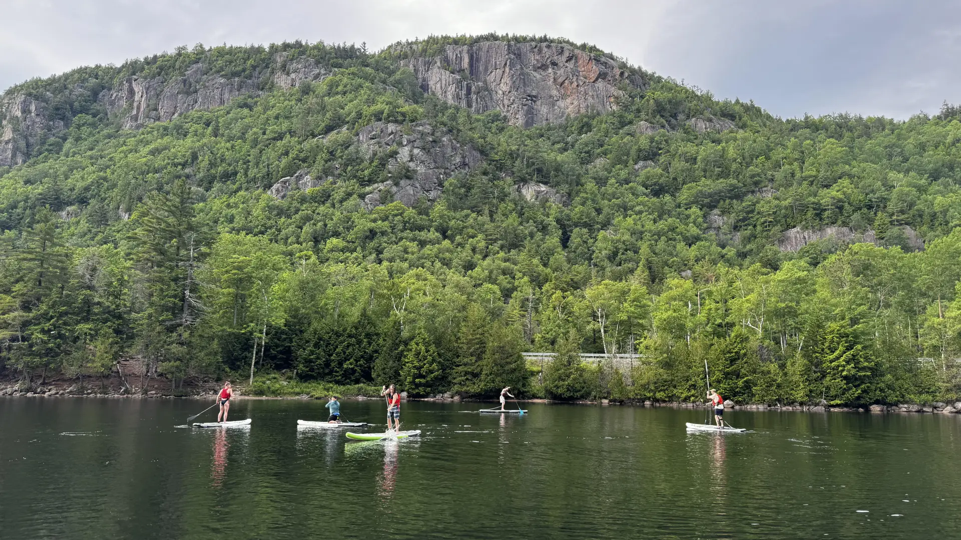 Five people are seen paddling on NRS paddle boards during a paddle clinic on Chapel Pond in the Adirondacks