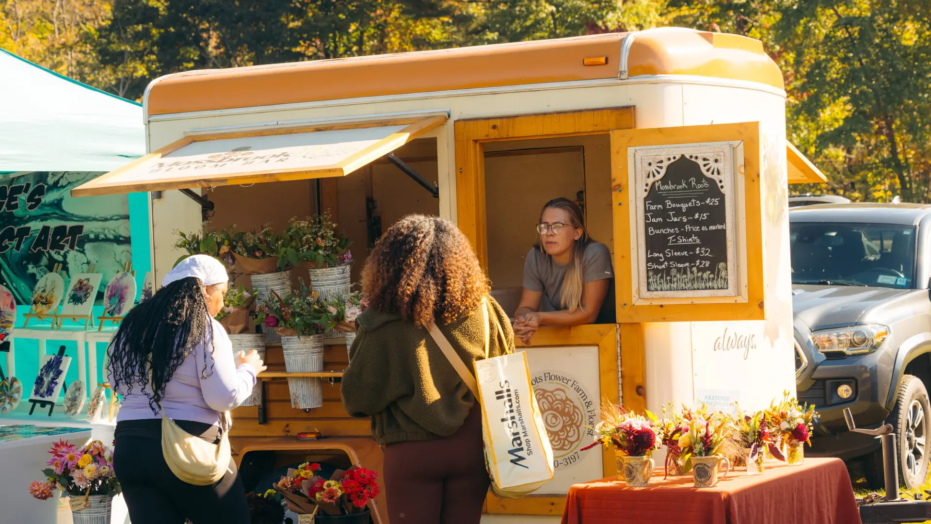 Two women visit a flower cart at a farmers market.